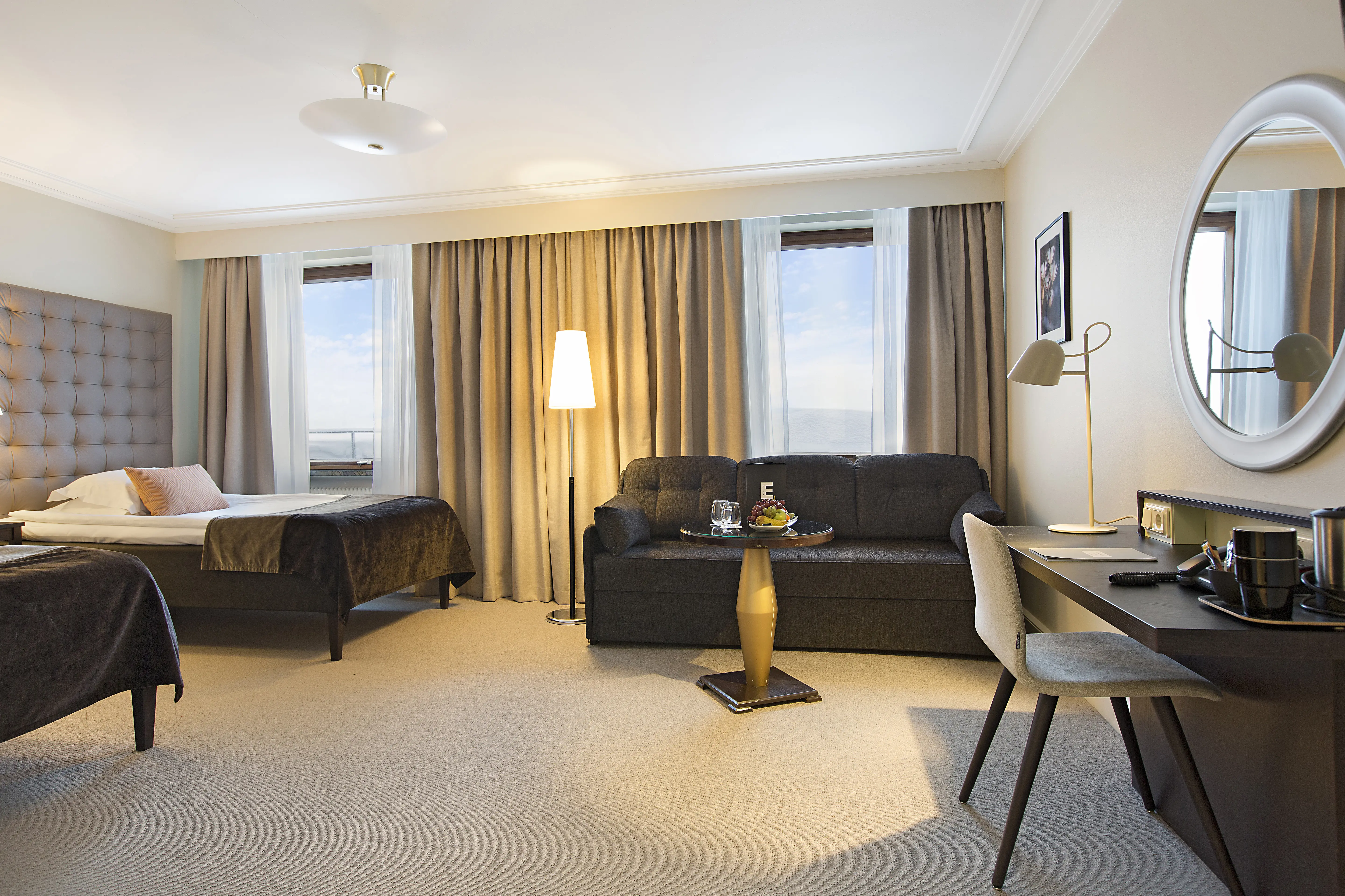 Ljust hotellrum med två sängar, soffa och skrivbord