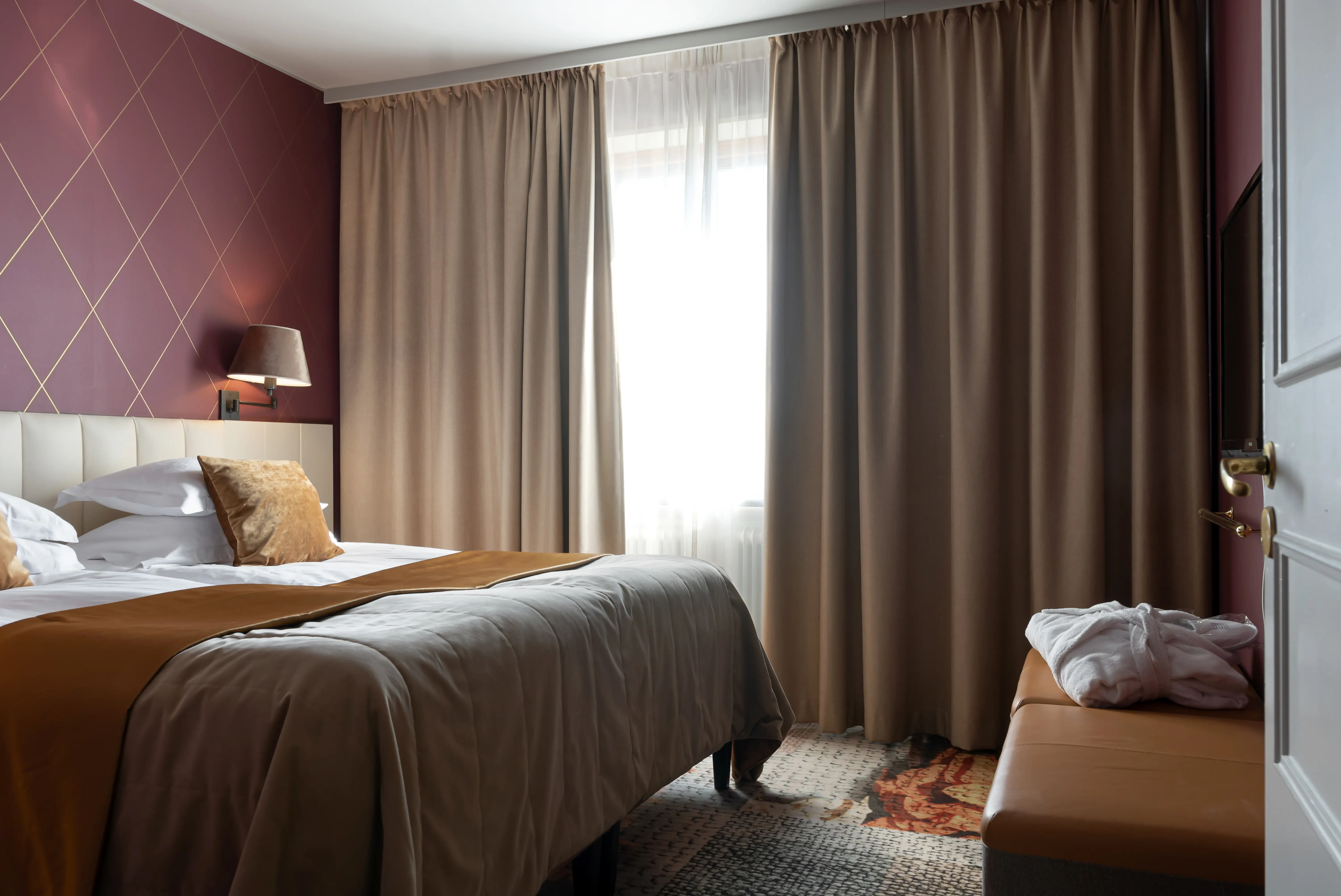 Svit med dubbelsäng, fönster och vinröda tapeter