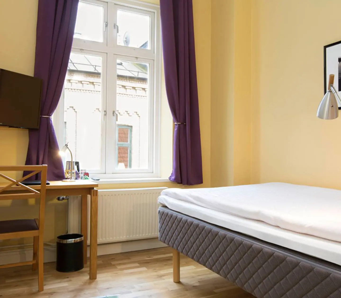 Gult hotellrum med säng, skrivbord och fönster