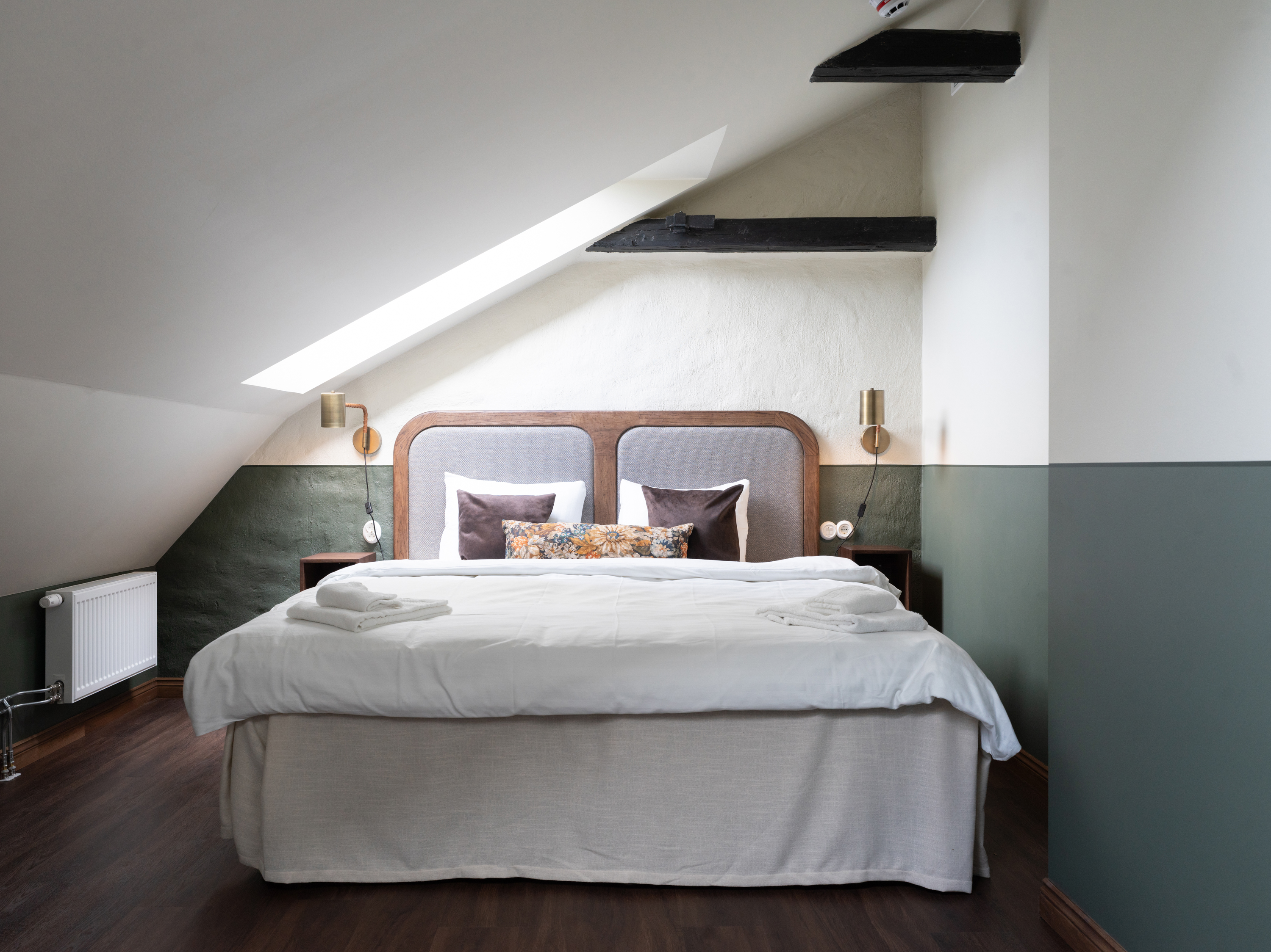 Sovrum i loftstil med dubbelsäng, mörkt trägolv och dämpad belysning under snedtak.