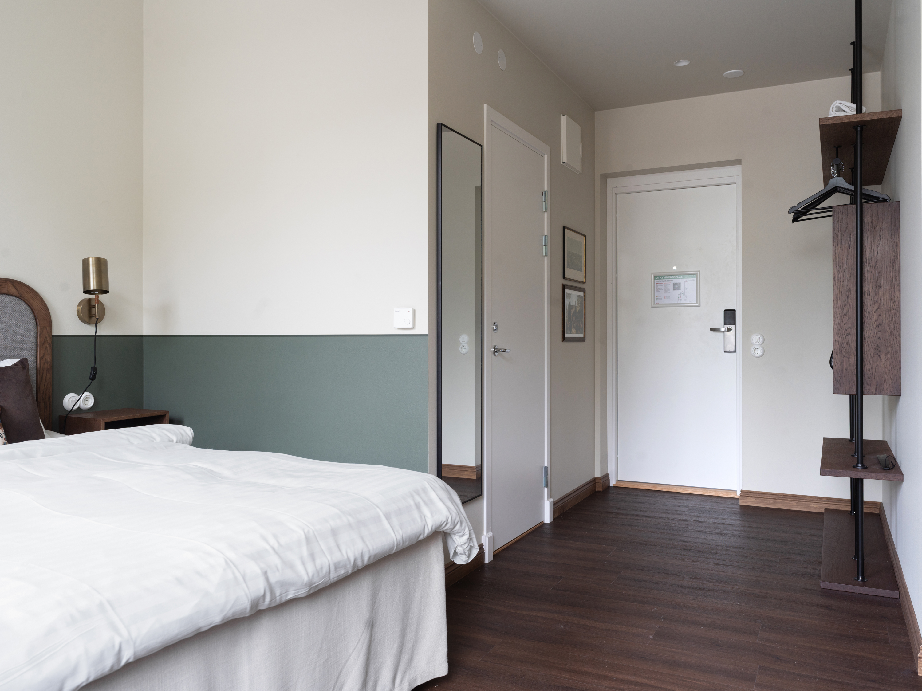 Ljust hotellrum med en dubbelsäng, träbord och stol, traditionell matta och konst på väggarna.