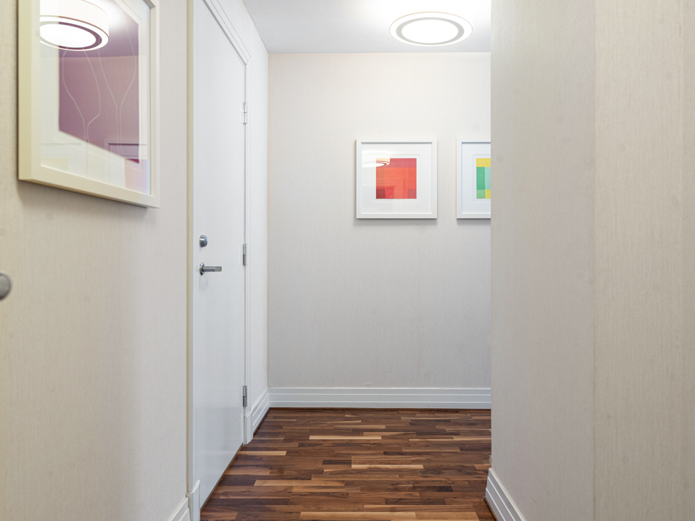 Ljus hall med vita väggar, trägolv och modern konst på väggarna.