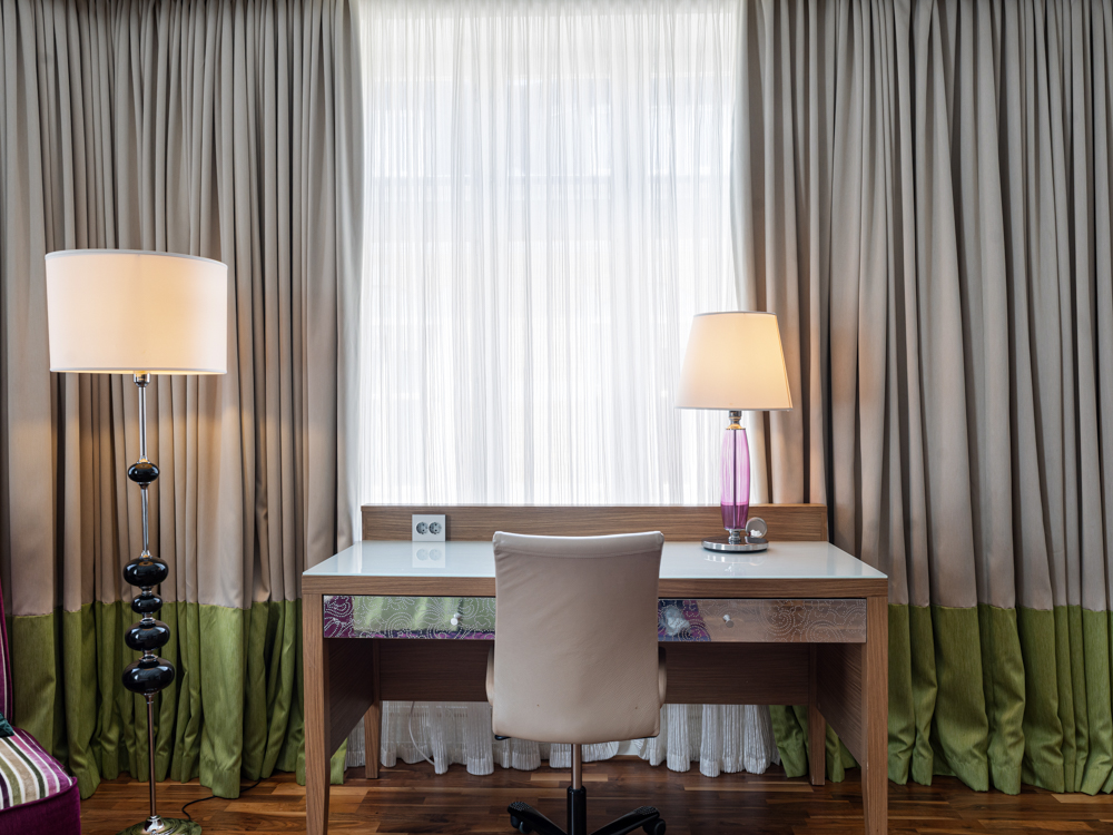 Arbetsplats vid fönster med skrivbordslampa och stol framför gardiner.