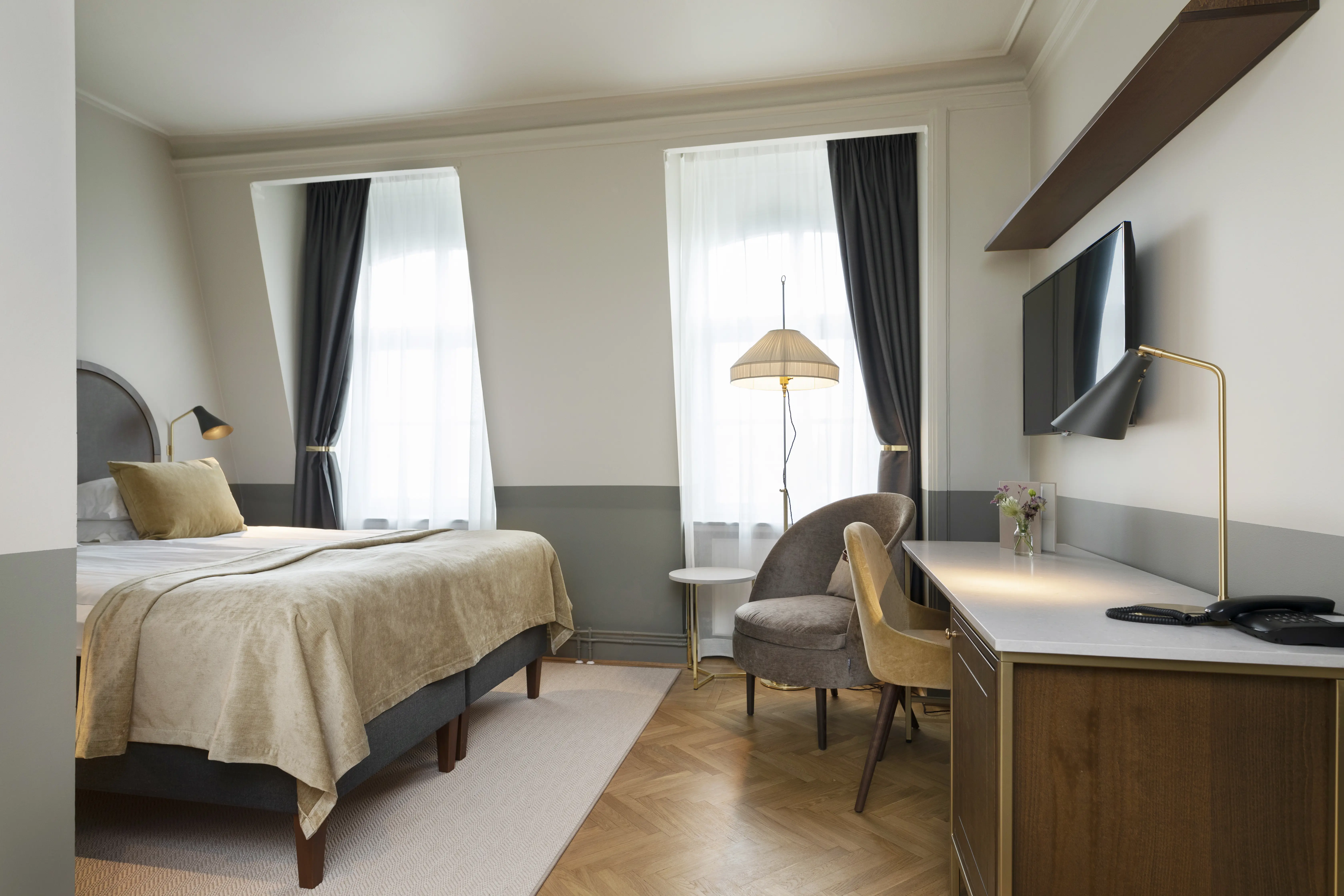 Ljust hotellrum med dubbelsäng, skrivbord, fåtölj och fönster