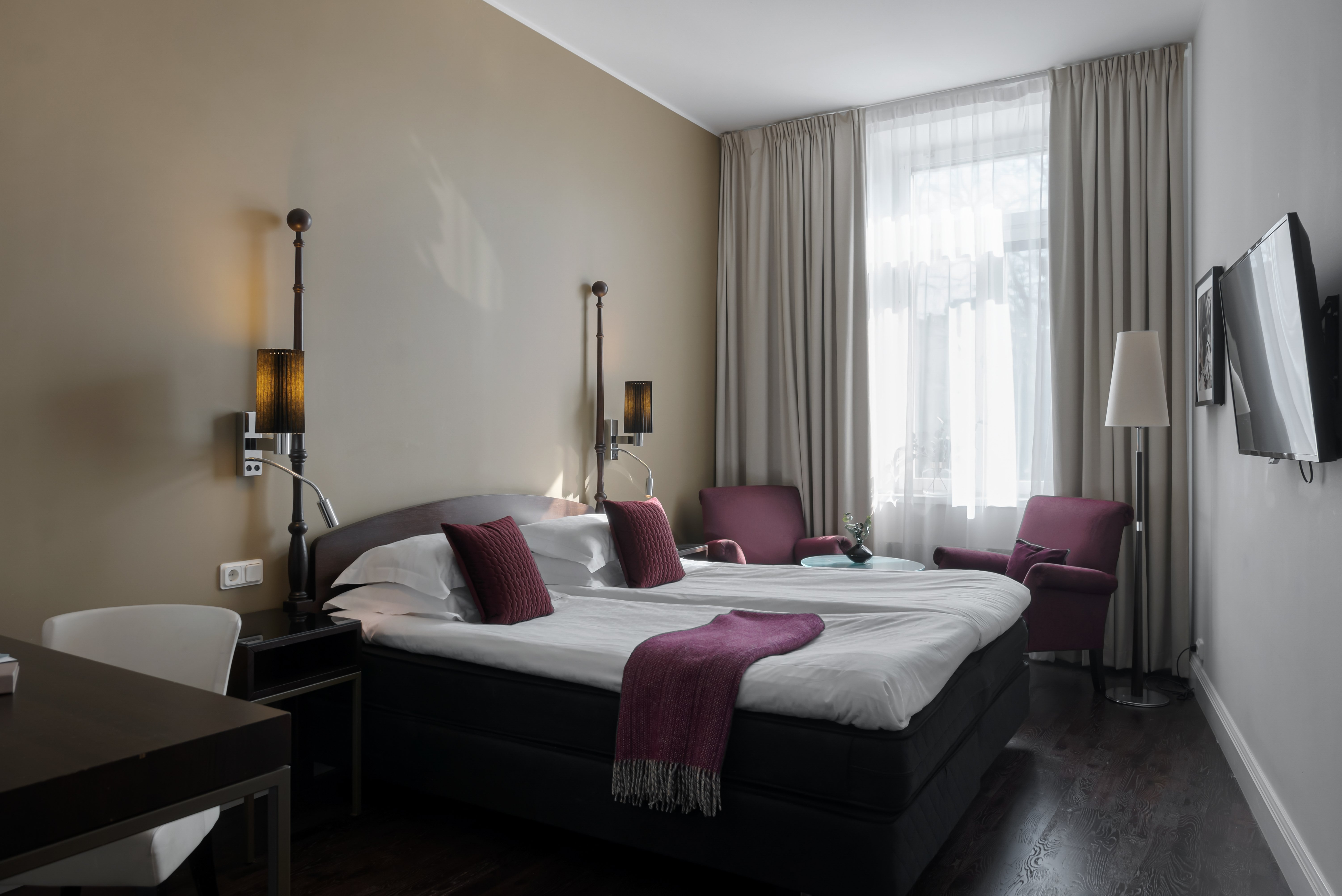 Bright hotel room with bed, purple armchairs and window