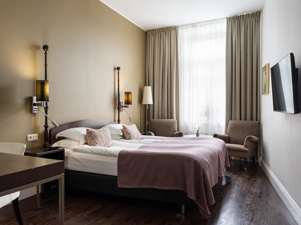 Bright hotel room with bed, purple armchairs and window