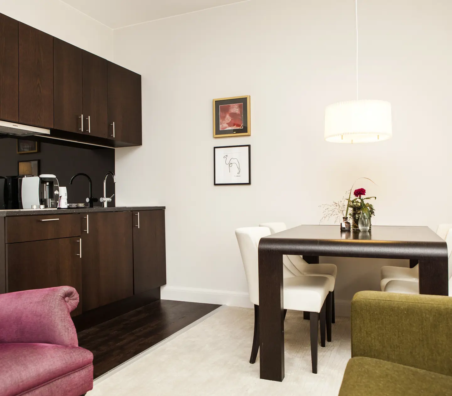 Modern minimalist room with dark wood table, white chairs, and kitchenette in a stylish urban apartment.