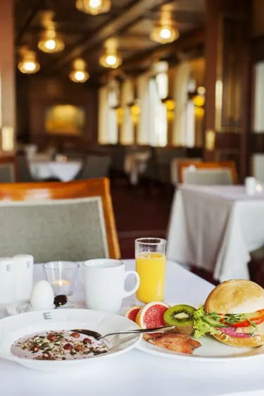 Breakfast buffet with yogurt and nuts, salmon, fresh fruit, orange juice, and a bread sandwich on a set table in an elegant dining room