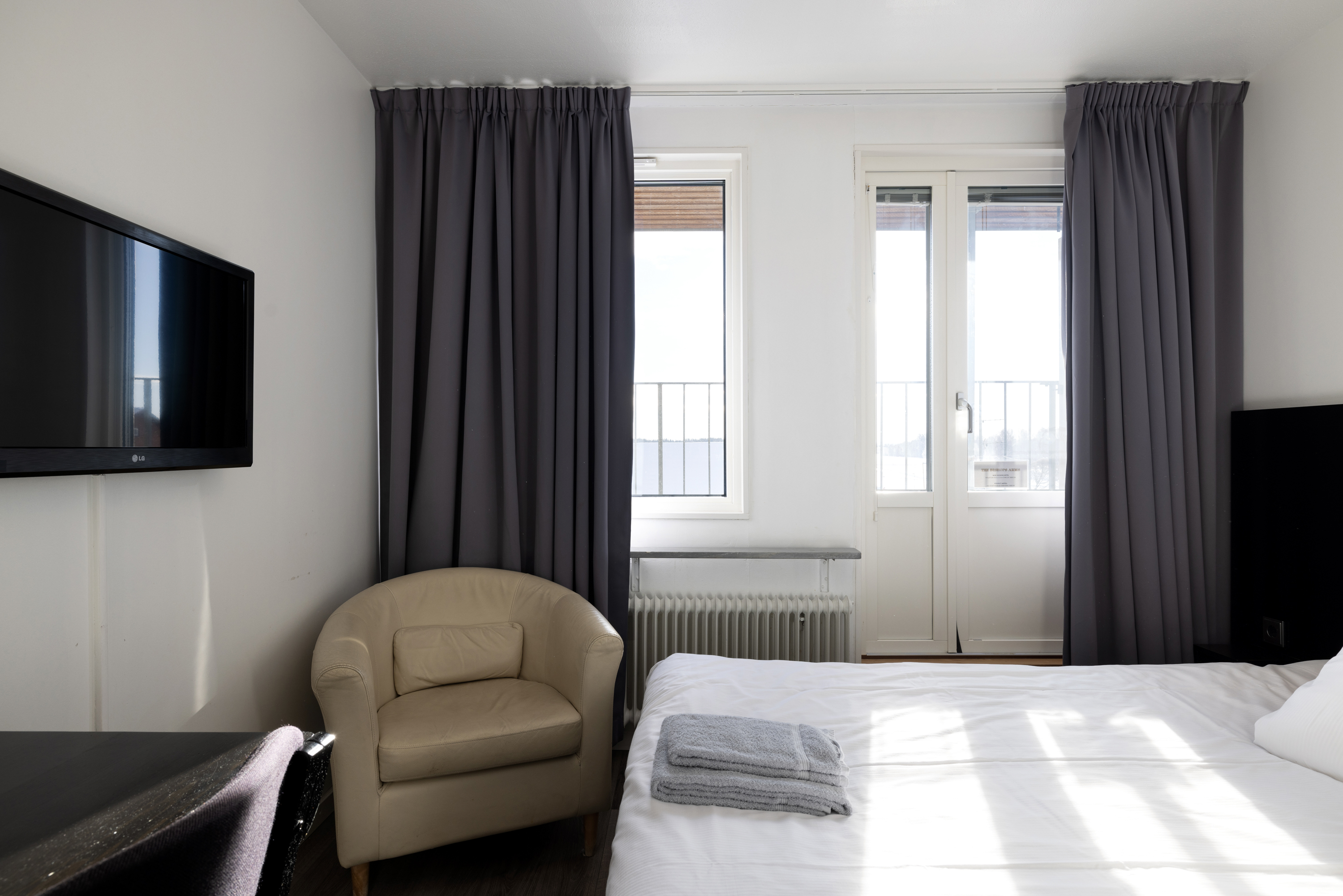 Hotellrum med säng, beige läderfåtölj och tv