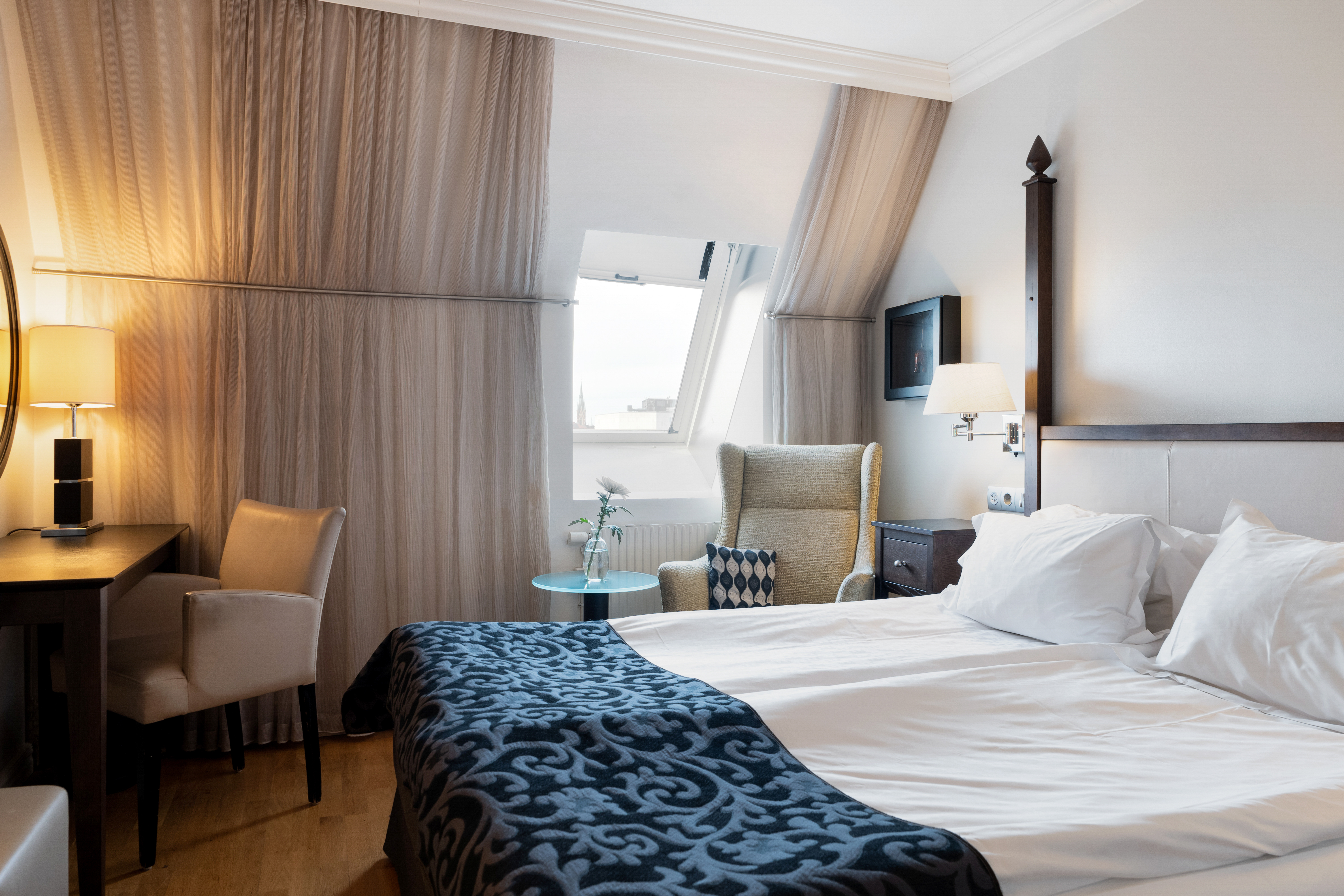 Bright hotel room with bed, desk and slanted ceiling