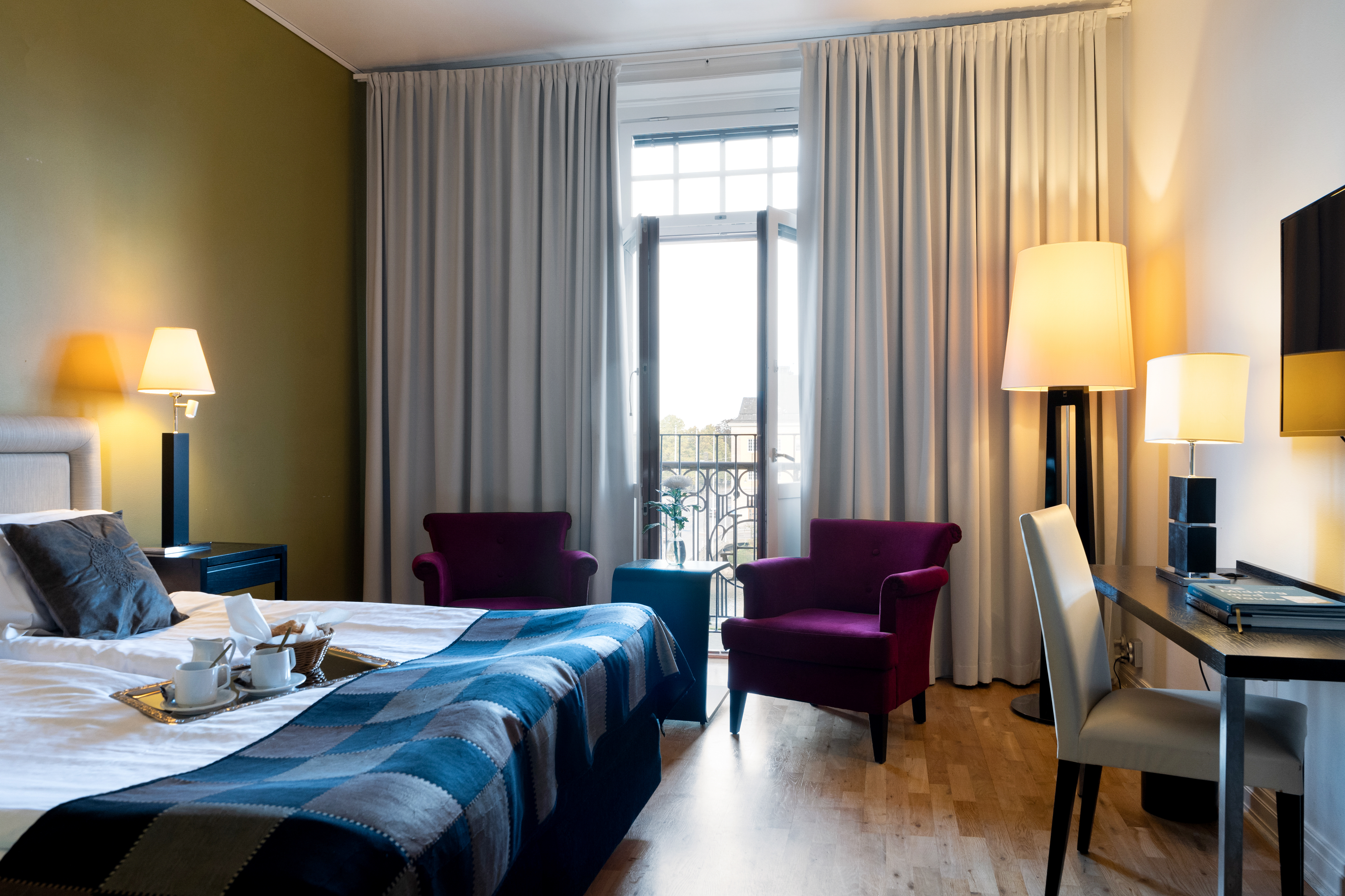 Bright hotel room with bed, desk and purple armchairs