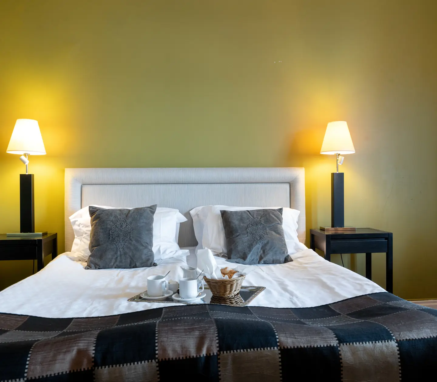 Hotellrum med gul vägg, säng och frukostbricka på sängen