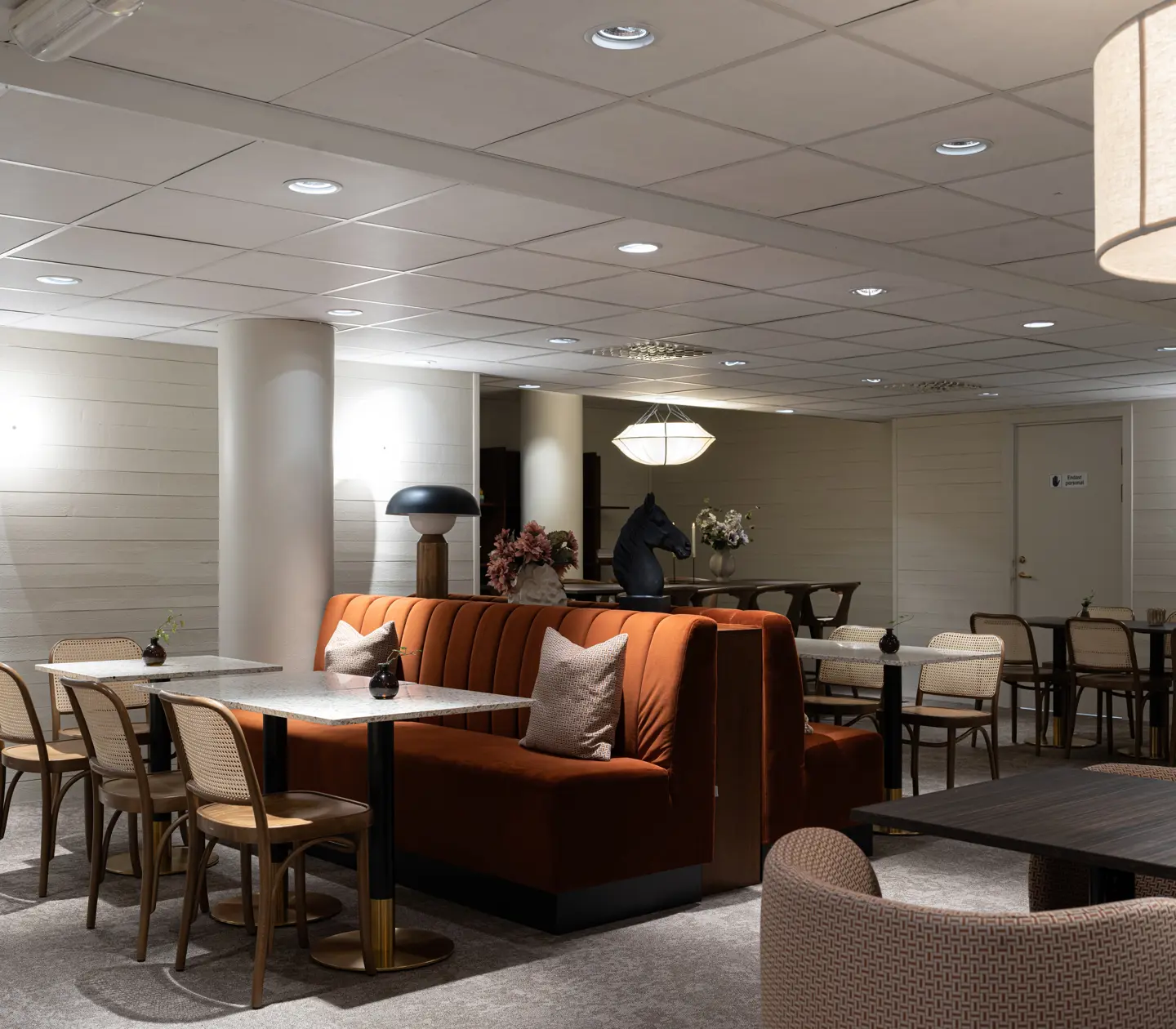 Stilren restauranginteriör med orange soffa, bord och stolar i trä, samt dämpad belysning