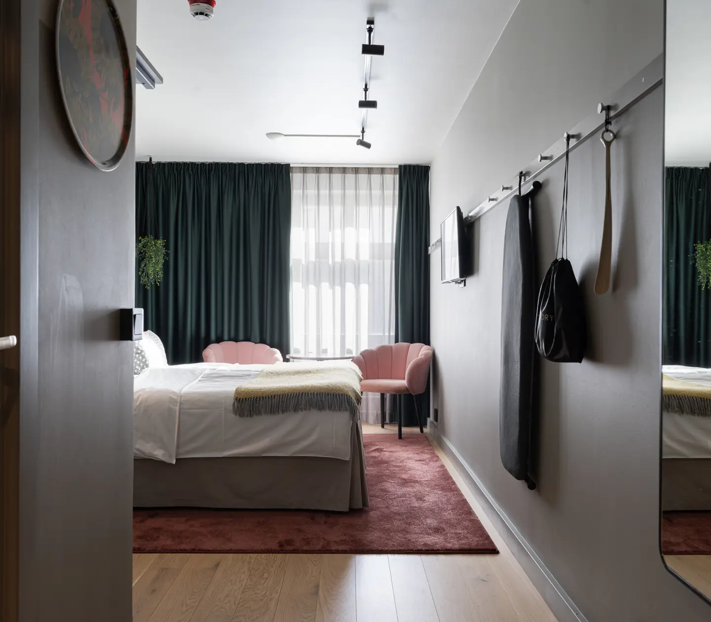 Modernt hotellrum med ljus inredning, säng med vita lakan, mörkgröna gardiner och rosa stolar
