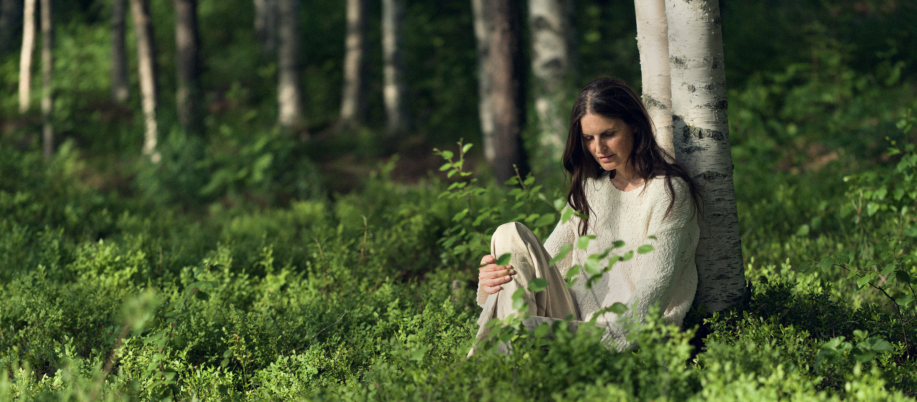 Kvinna som lutar sig mot ett träd i en lummig skogsmiljö