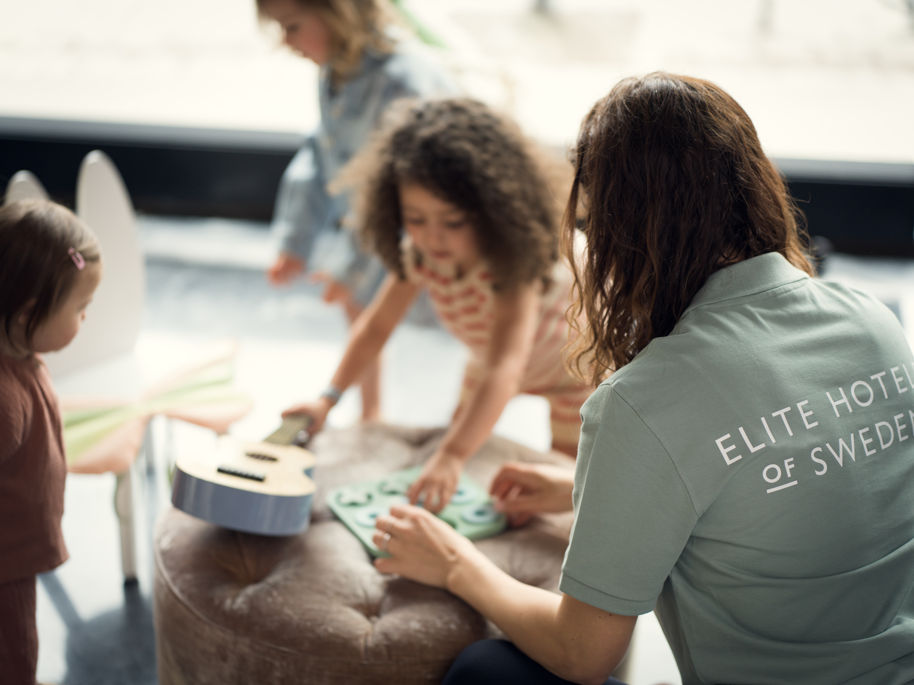 Barn leker med ett trätåg på ett golv, omgiven av mjuka leksaksdjur i ett mysigt rum.