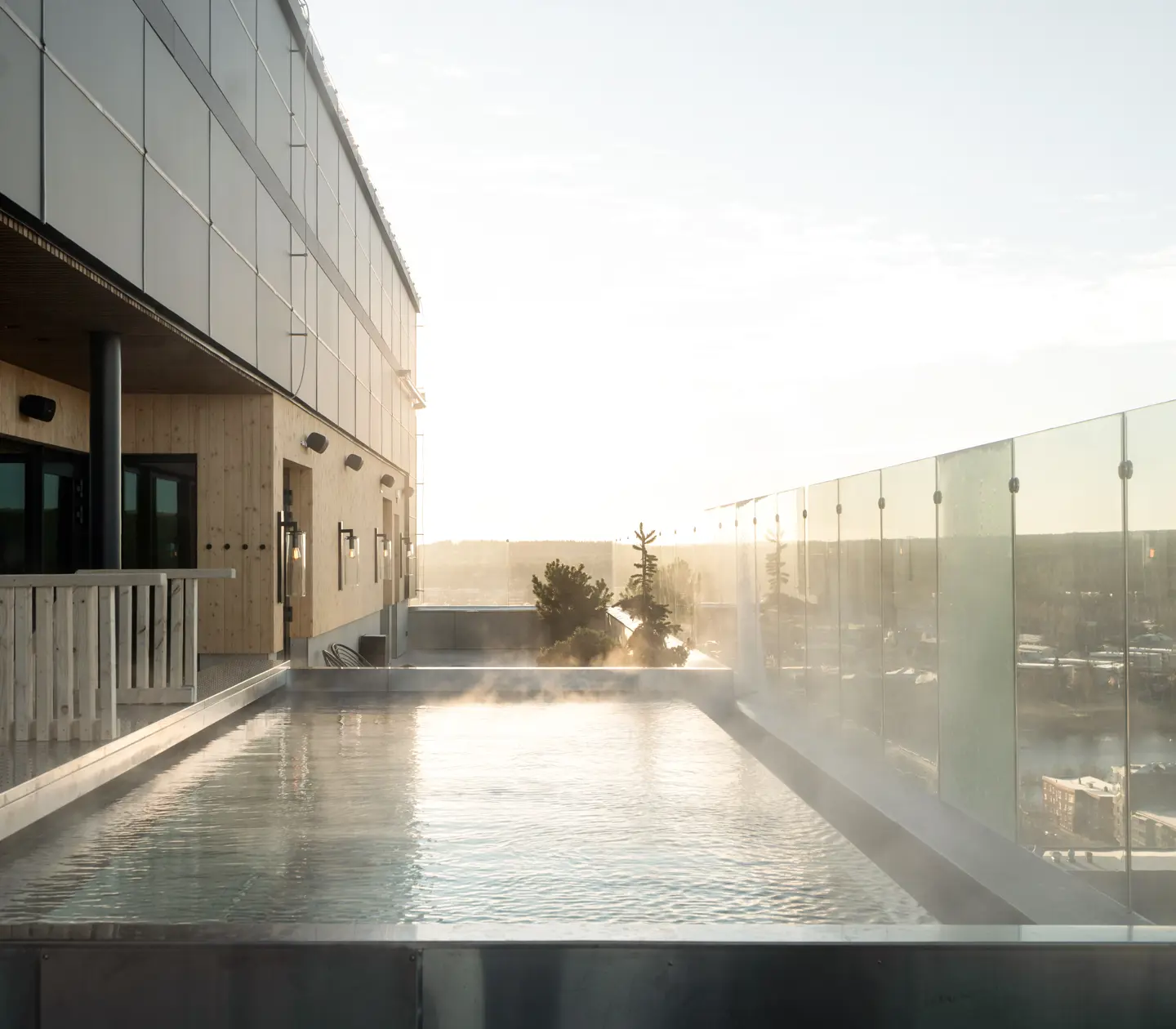 Outdoor pool with steam above the water surface, glass railing and view of Skellefteå