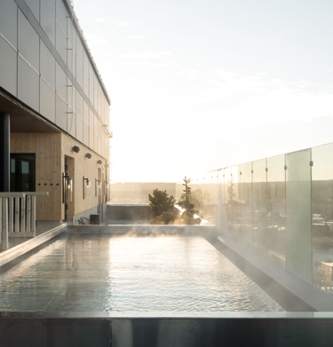 Outdoor pool with steam above the water surface, glass railing and view of Skellefteå