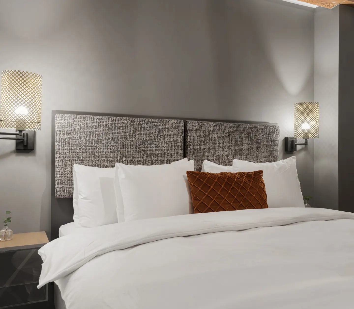 Ljust hotellrum med säng, grå sänggavel och sänglampor