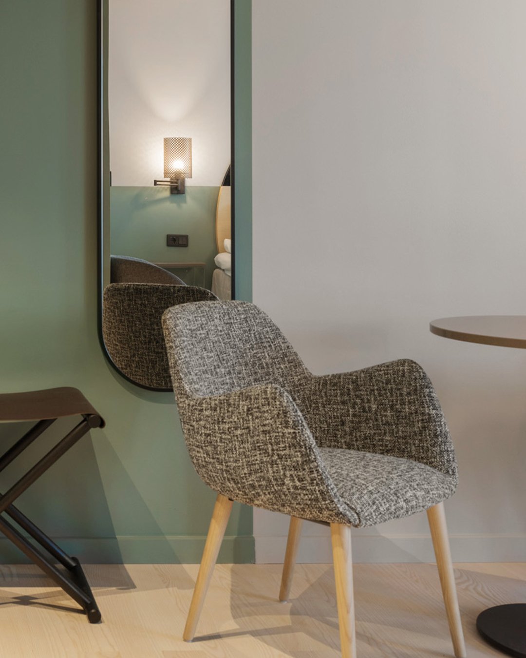 Bright hotel room with armchair, green and white wall and mirror