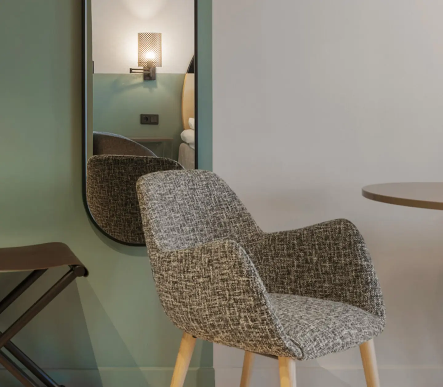 Ljust hotellrum med fåtölj, grön och vit vägg och spegel