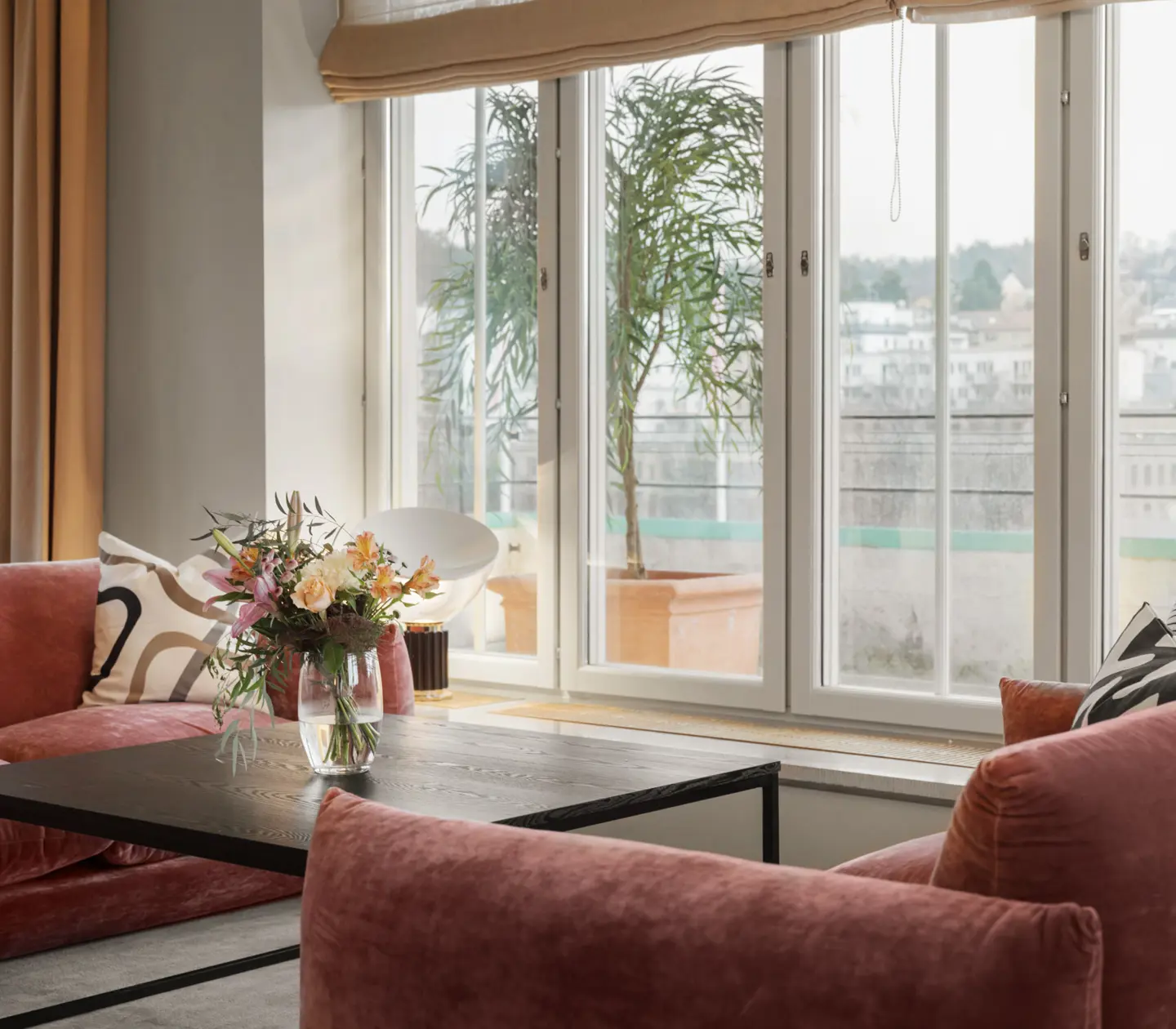 Mysig svit med rosa soffgrupp, blombukett och fönster längs väggarna