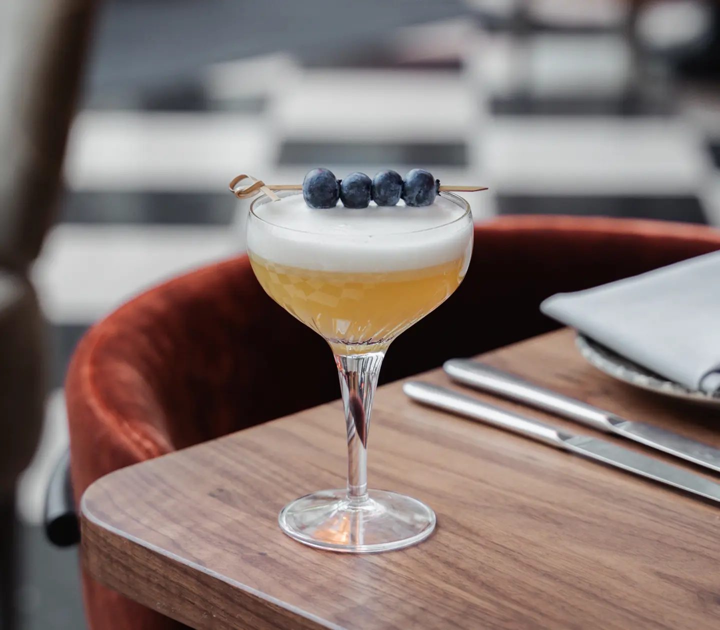 Yellow drink served on table with blueberry on stick on top of glass