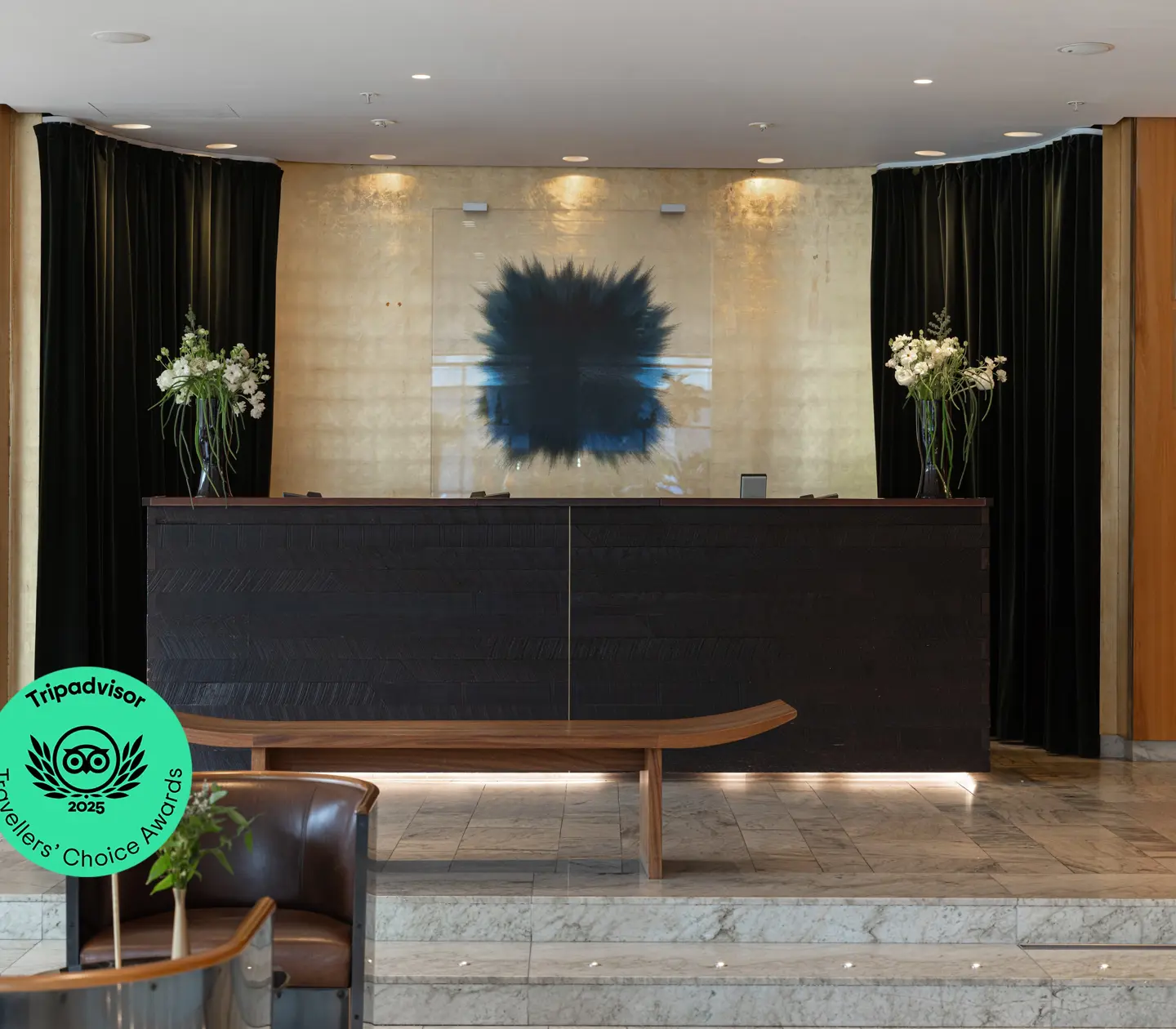 Receptionen på ett modernt hotell med mörkt träskranka, marmorgolv och blomsterarrangemang.
