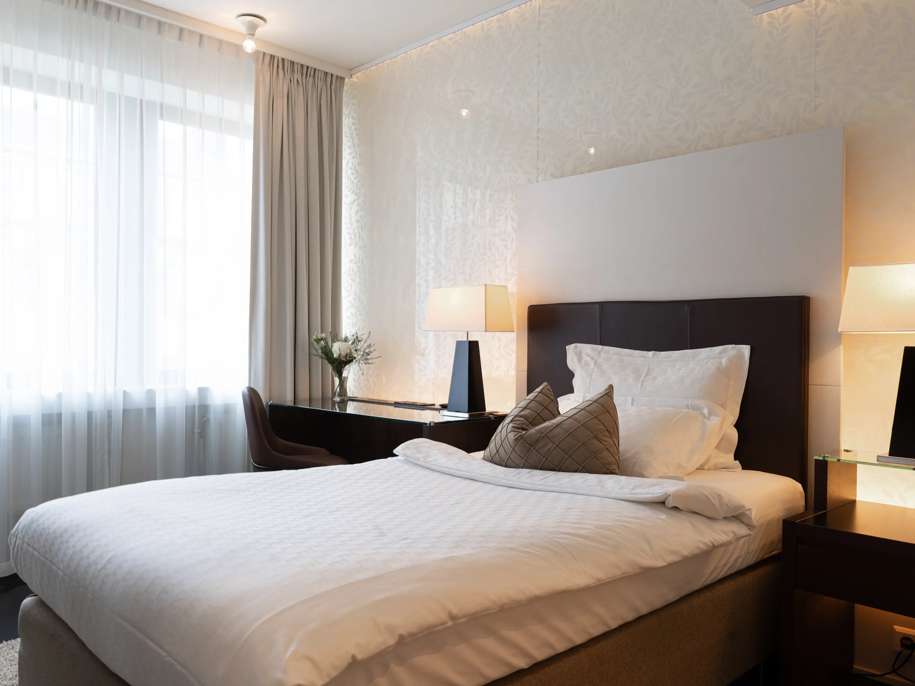 Ljust hotellrum med säng, skrivbord och fönster