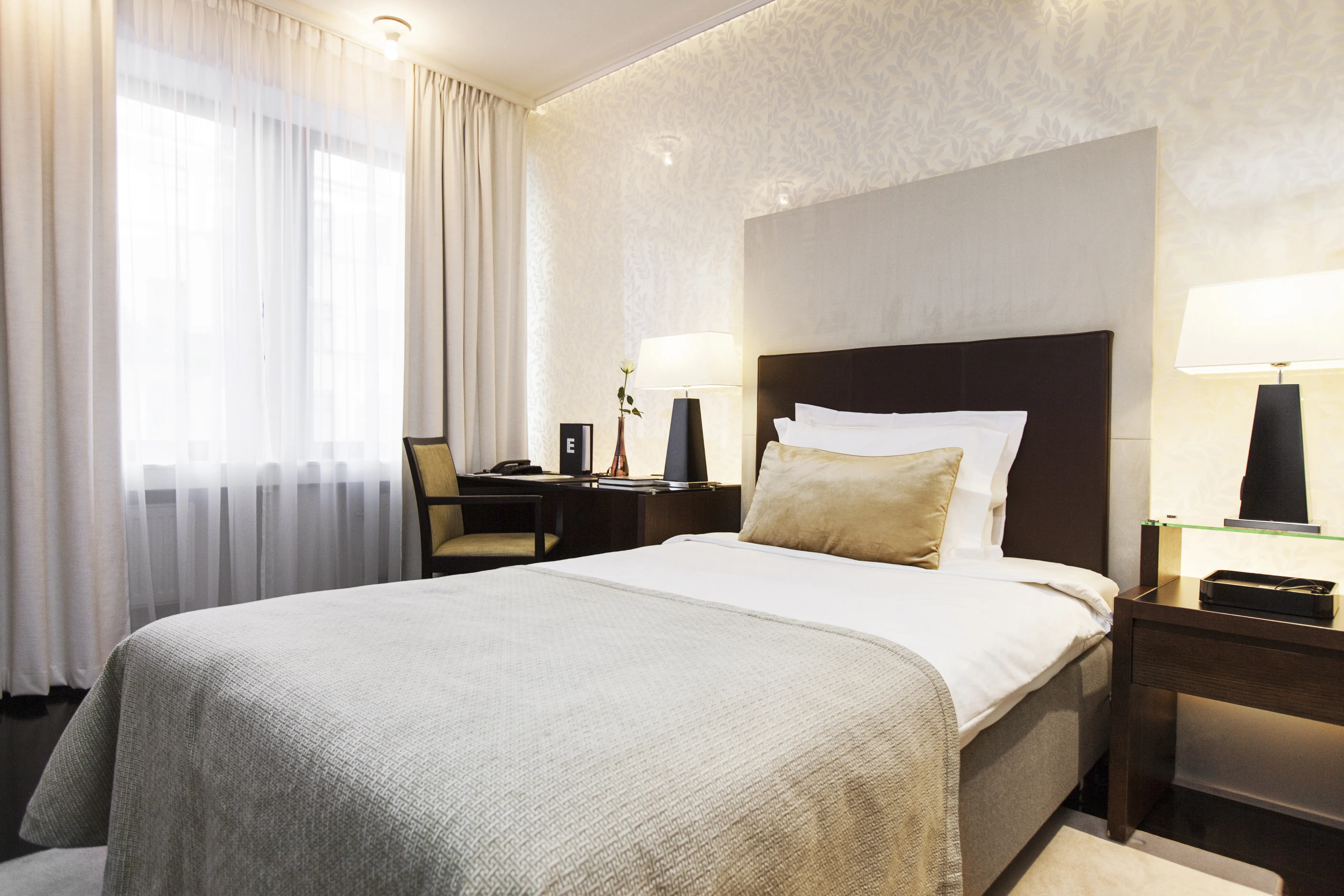 Ljust hotellrum med säng, skrivbord och fönster