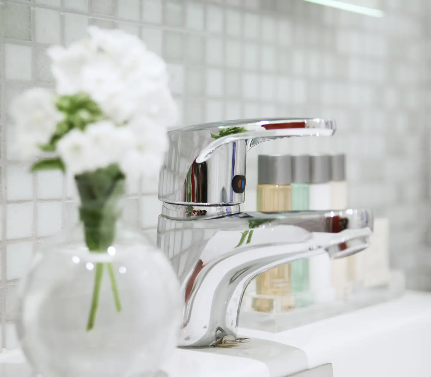 Detail of faucet in bathroom with flower in the foreground and small bottles in the background
