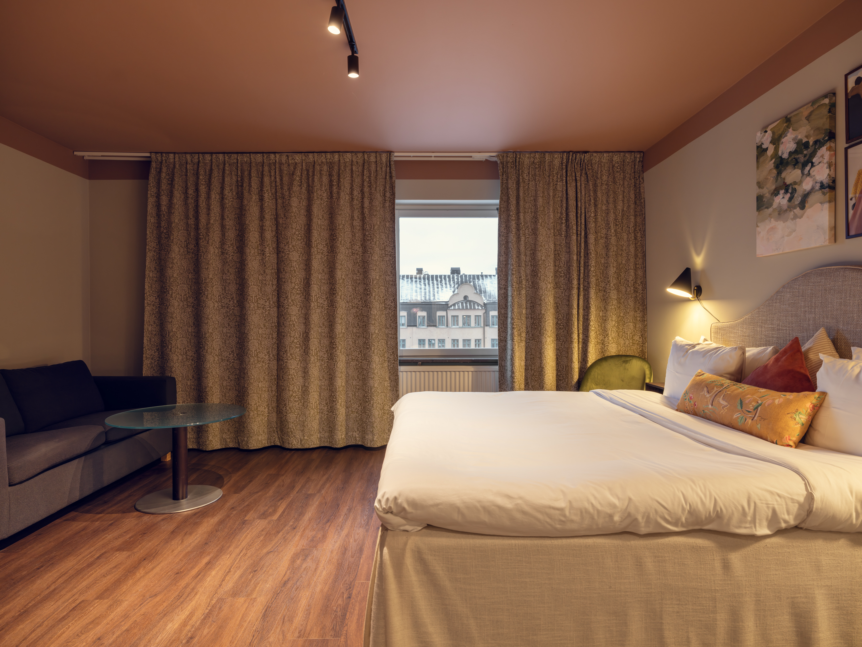 Ljust hotellrum med säng, tavlor och fåtöljer