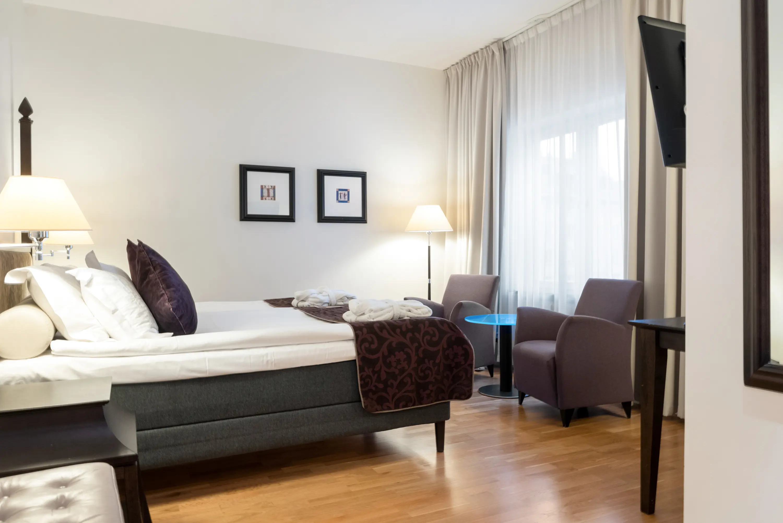 Ljust hotellrum med säng, tavlor och fåtöljer