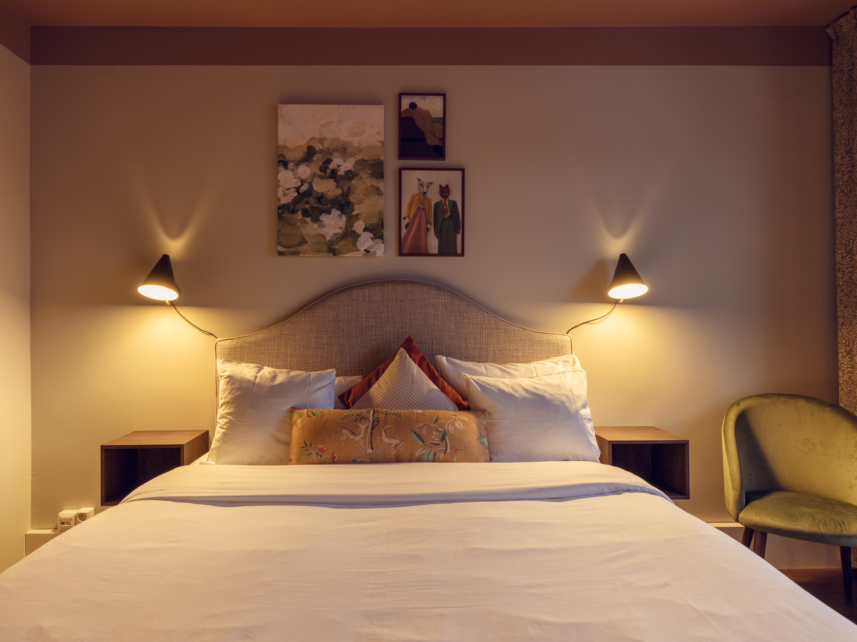 Ljust hotellrum med säng, fåtöljer och gardiner