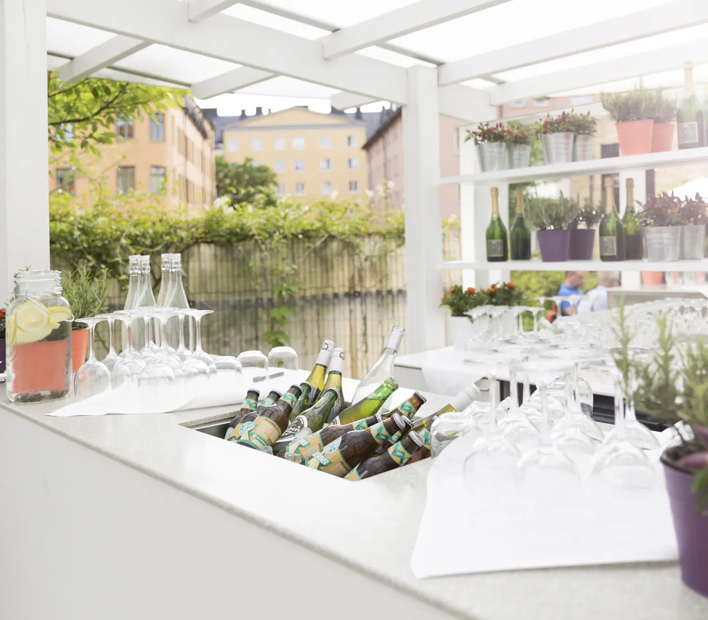 Bright outdoor bar with bottles, glasses and greenery in the background