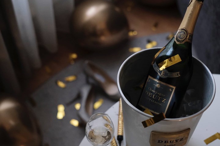 Champagneflaska i ishink med glas i förgrunden, omgiven av festlig konfetti och guldiga dekorationer.