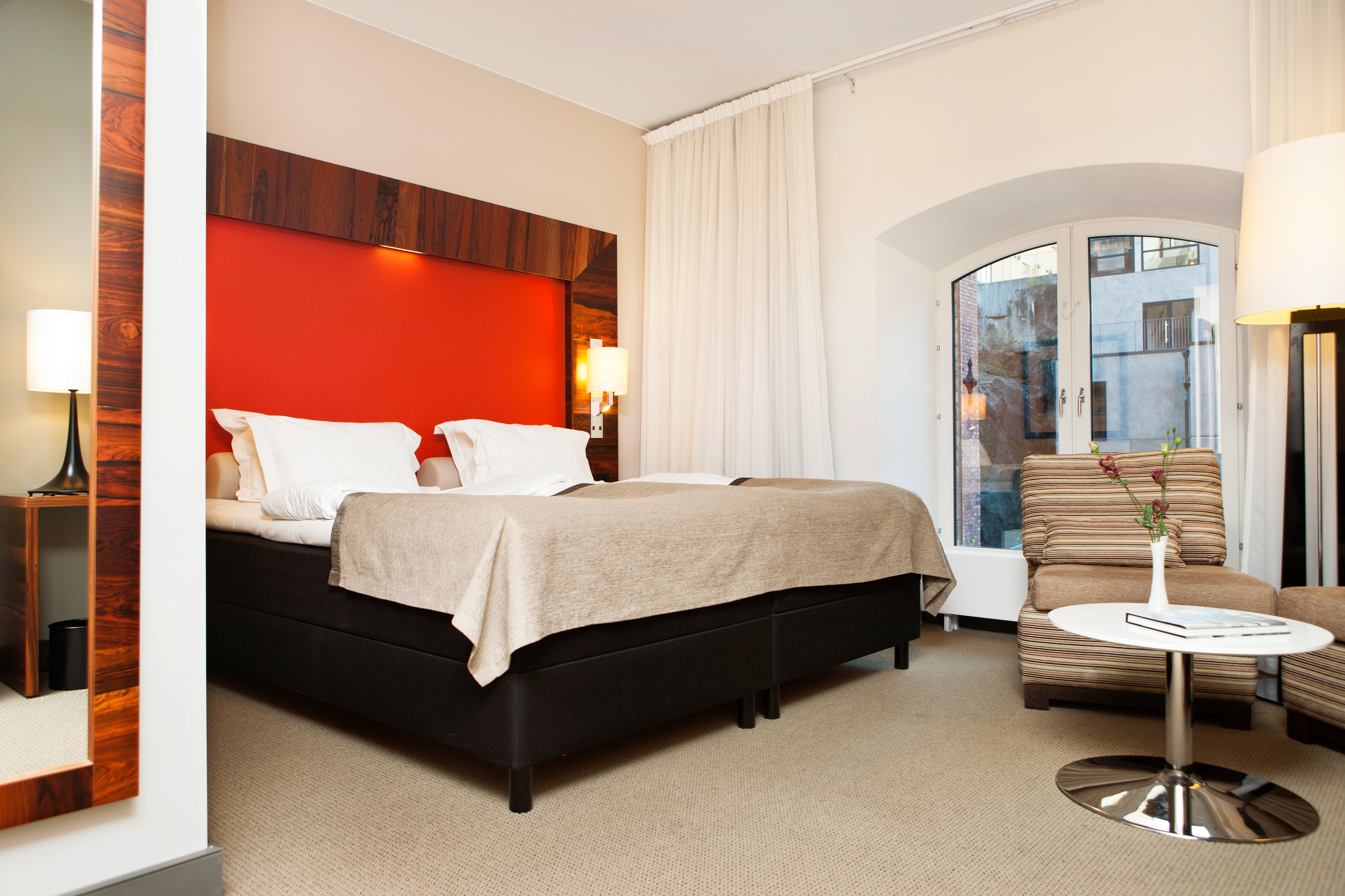 Bright hotel room with bed, red headboard and armchairs
