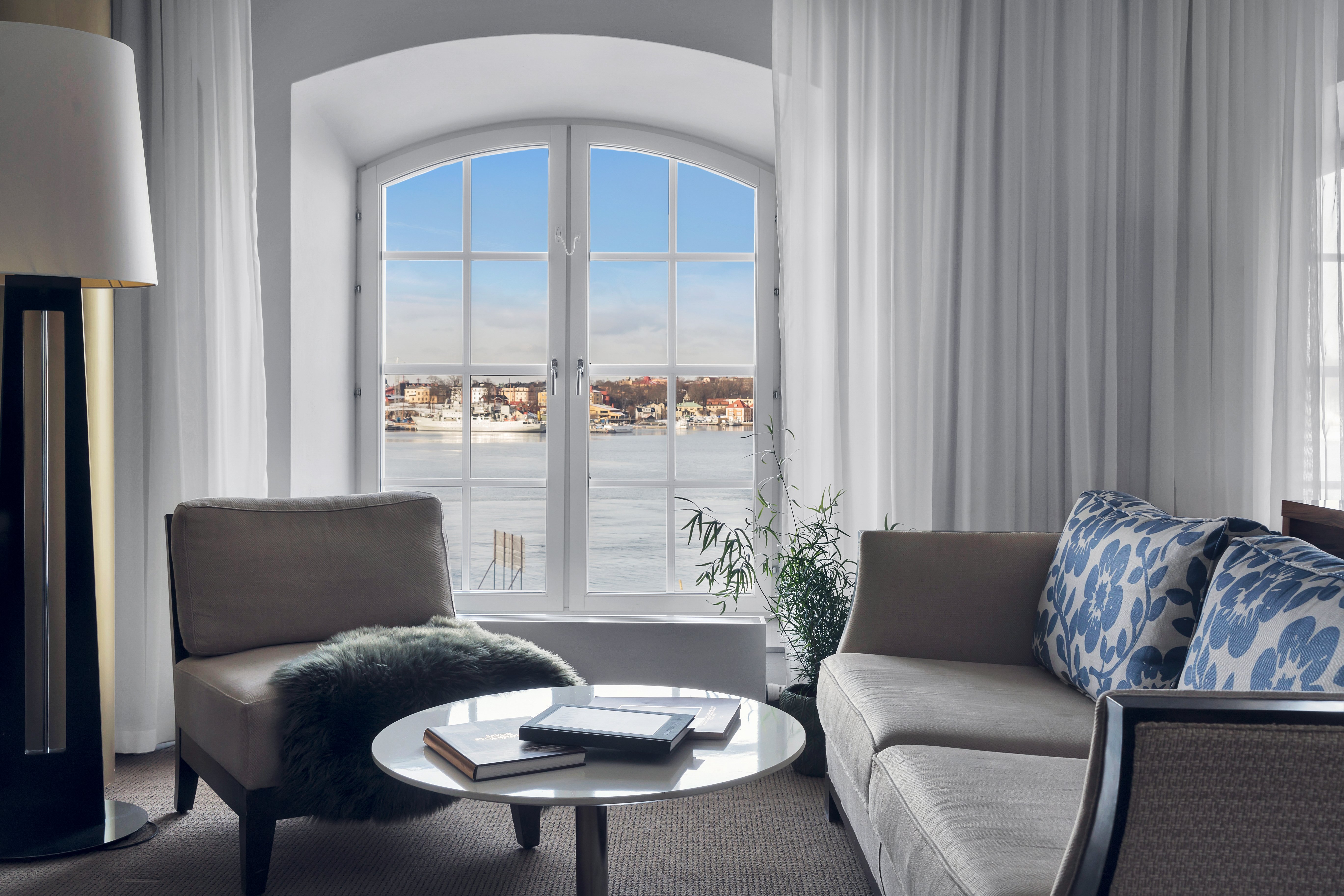 Bright hotel room with sofa group, floor lamp and window with sea view