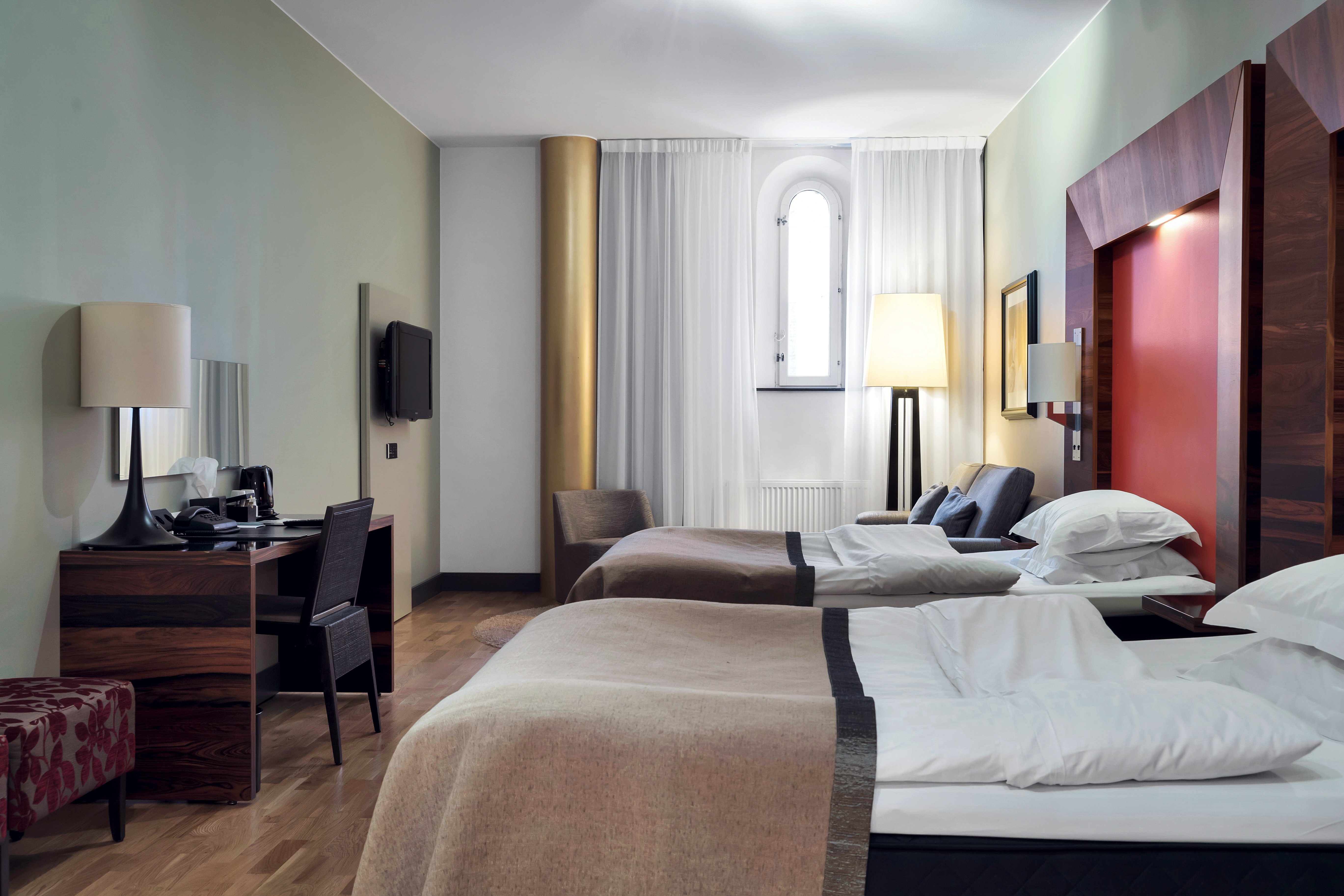 Bright hotel room with beds, red headboards and desk