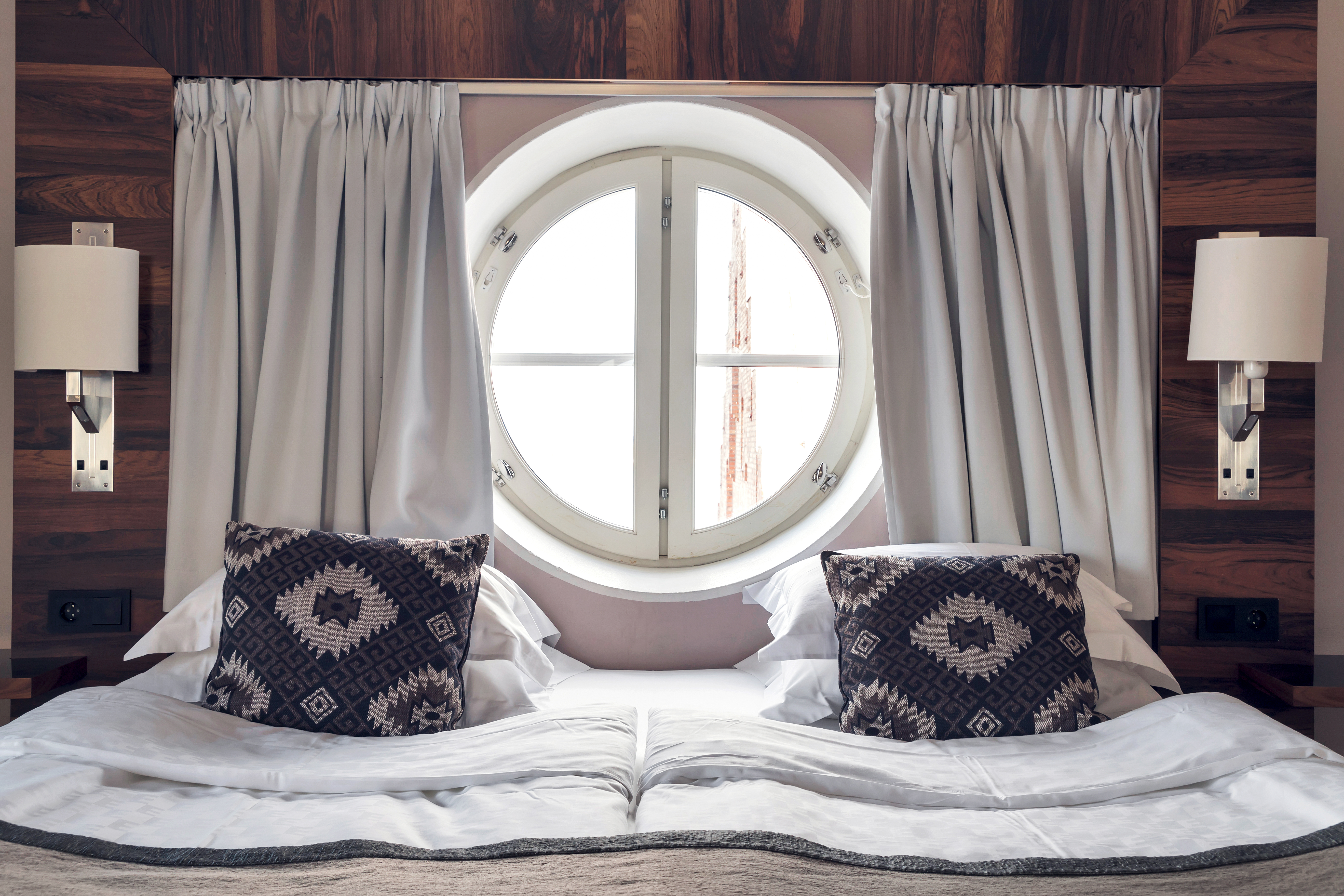 Bright suite with round window in front of bed and curtains