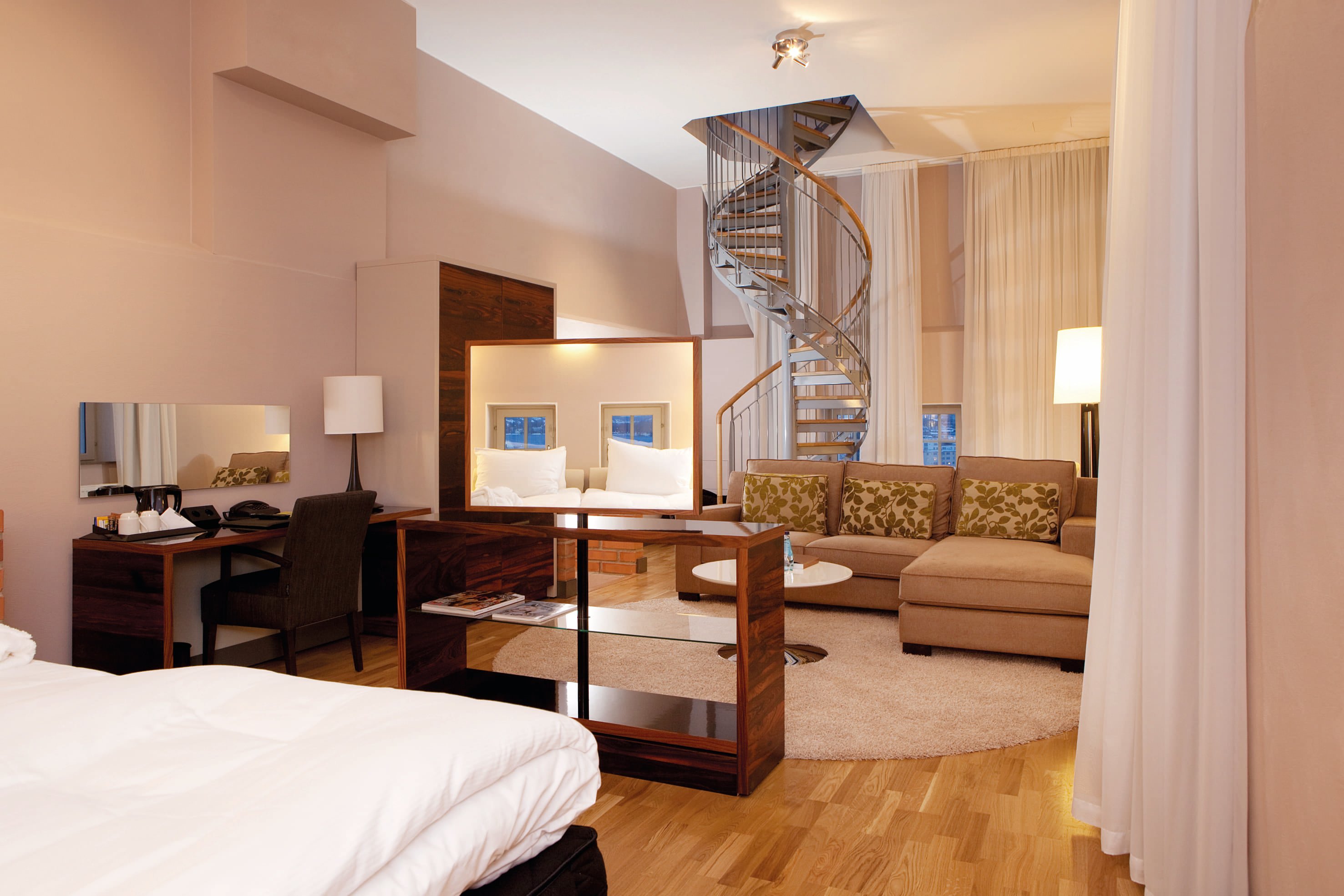 Modern hotel room with spiral staircase, cozy seating area, and soft lighting, featuring a plush bed, wooden furniture, and contemporary decor