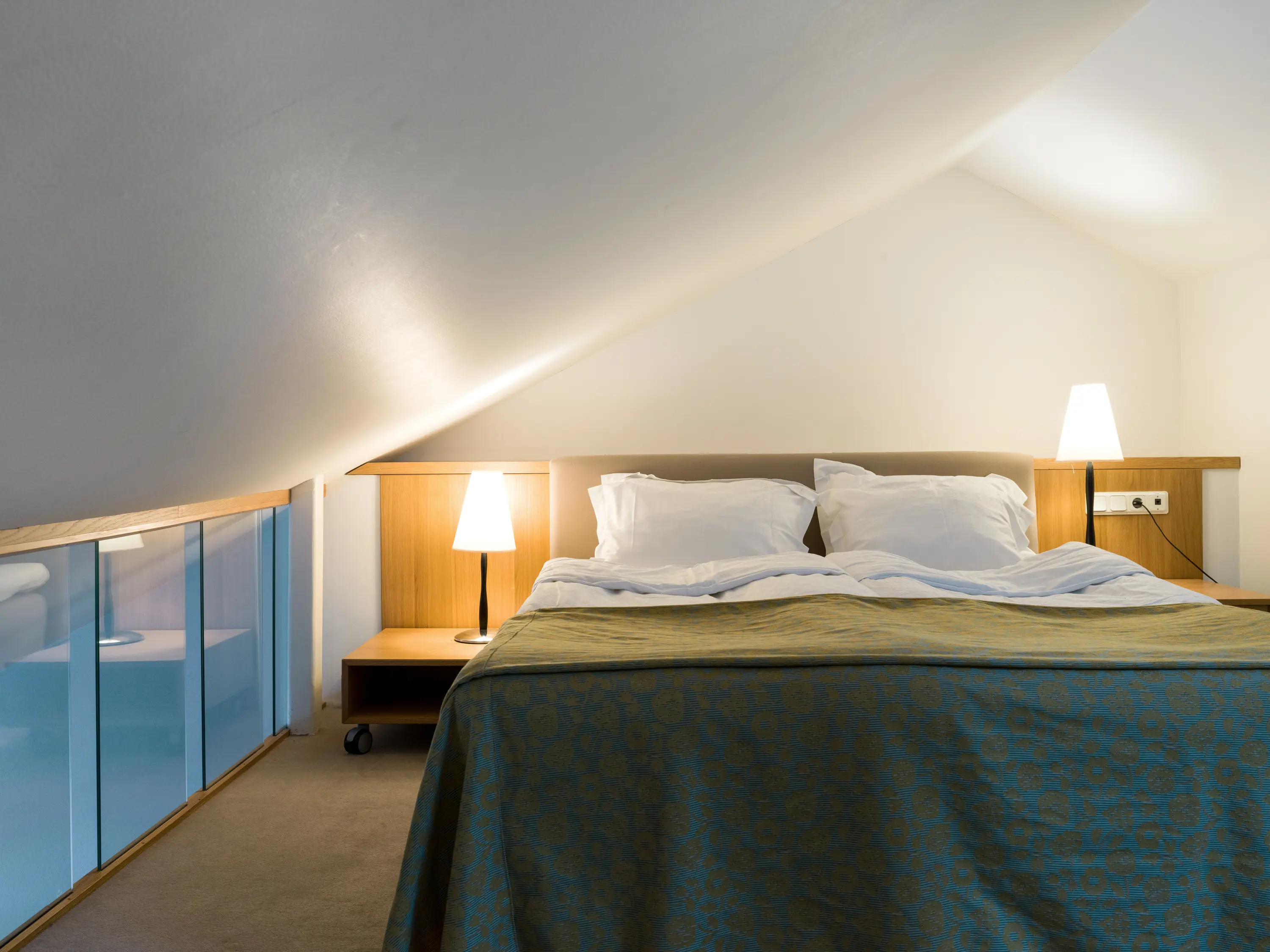 Ljust hotellrum med säng, glasräcke och sänglampor
