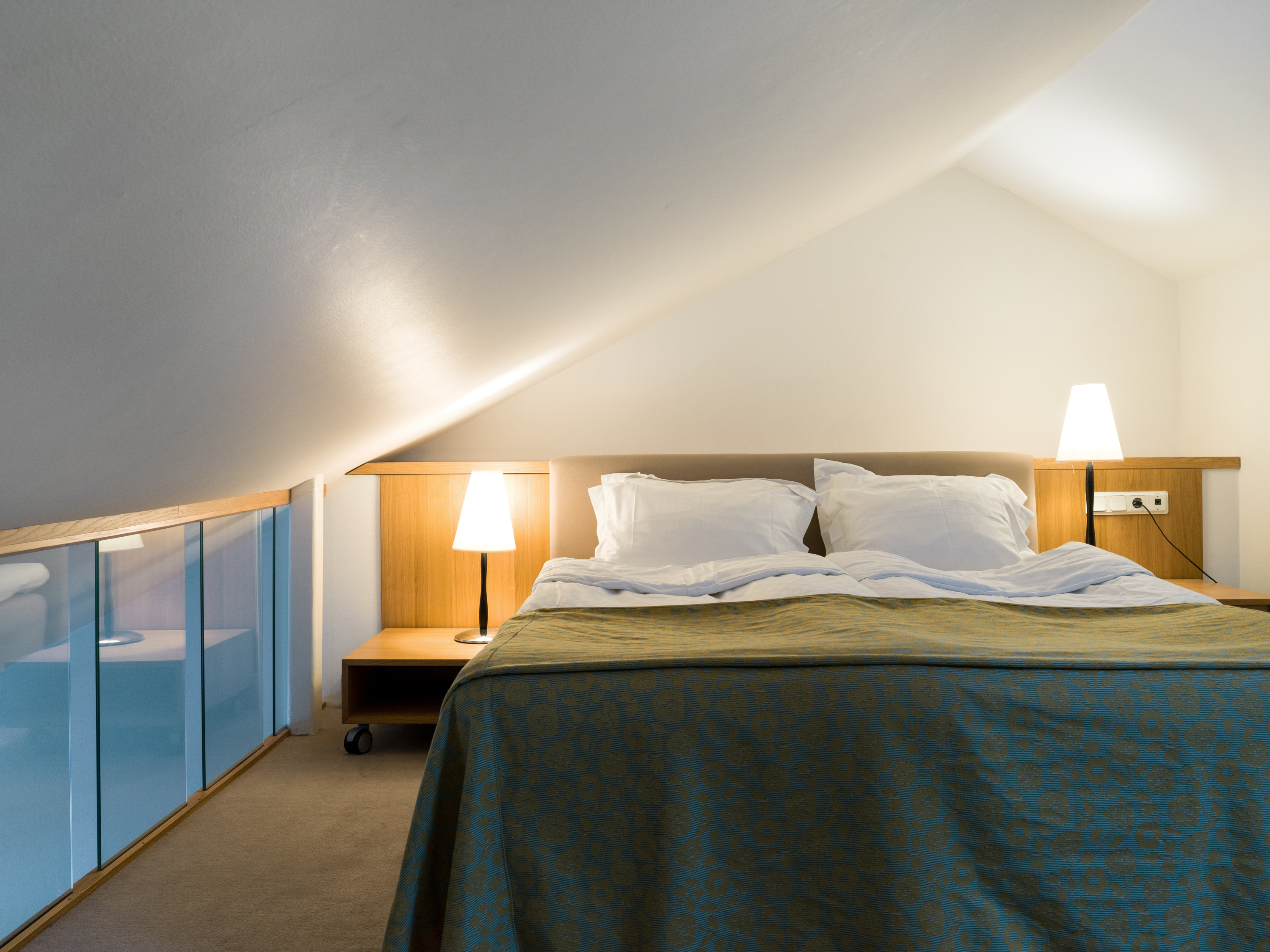 Bright hotel room with bed, glass railing and bedside lamps