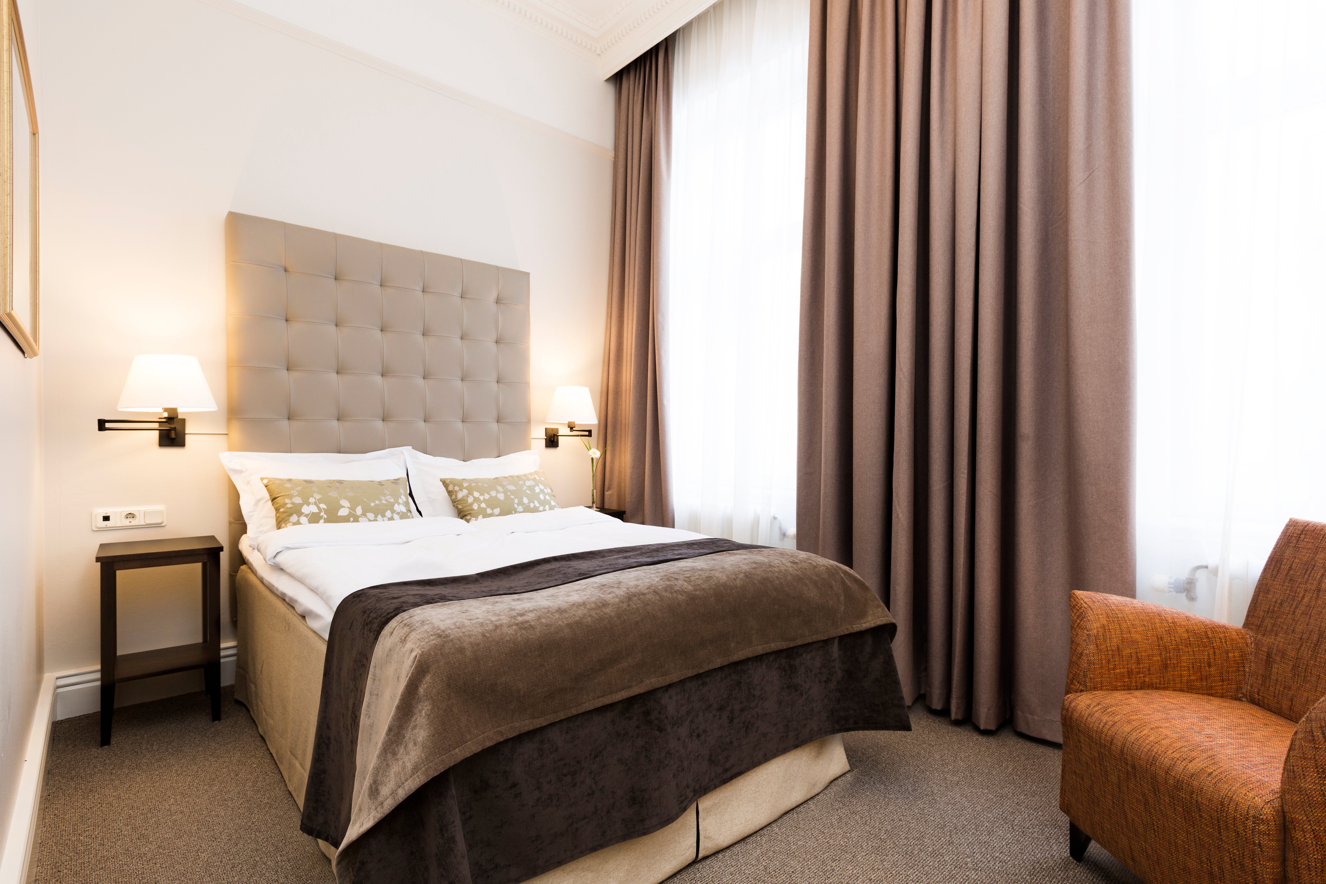 Bright hotel room with bed, gray headboard and armchair