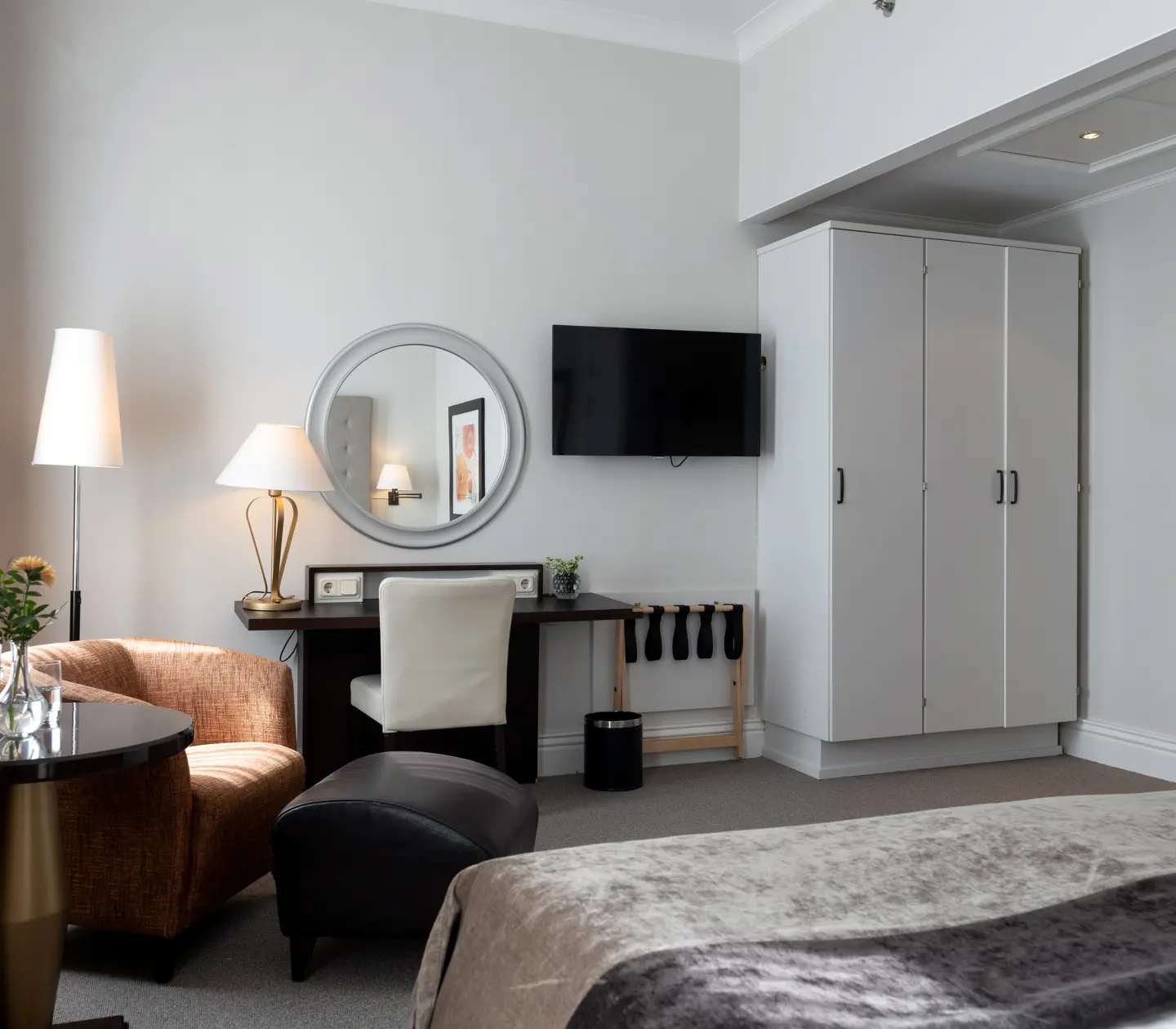 Ljust hotellrum med rund spegel, garderob och fåtölj