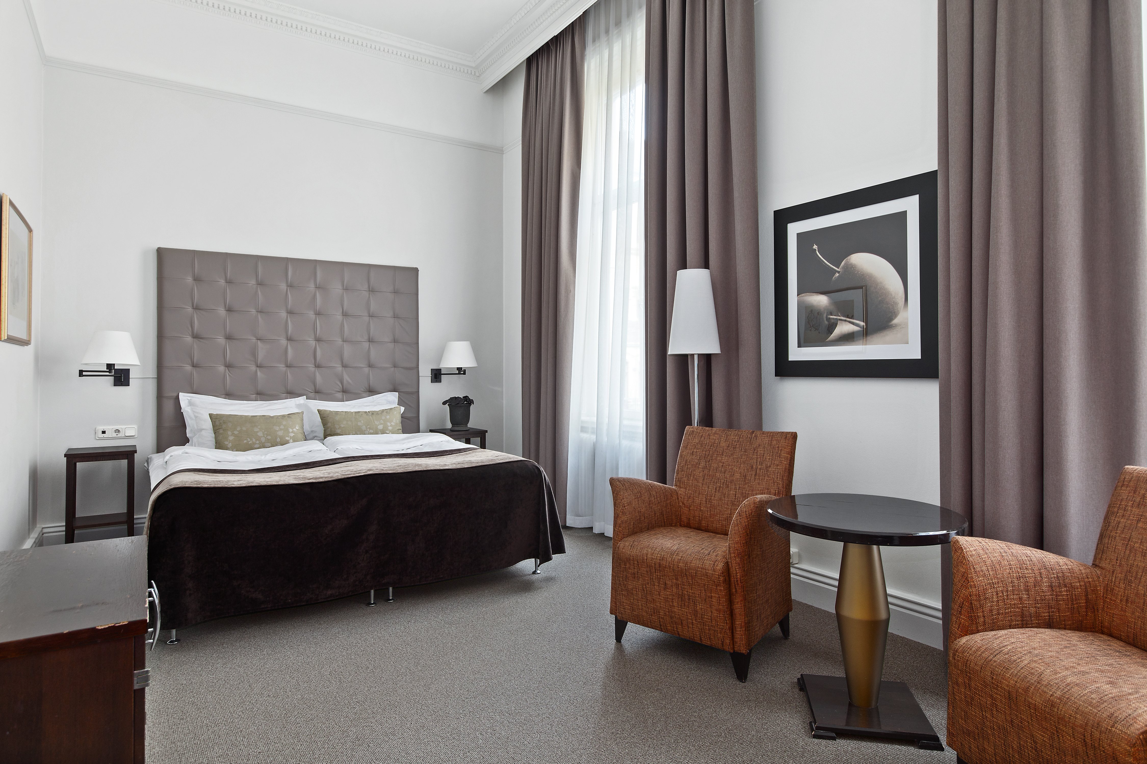 Bright hotel room with bed, gray headboard and armchairs