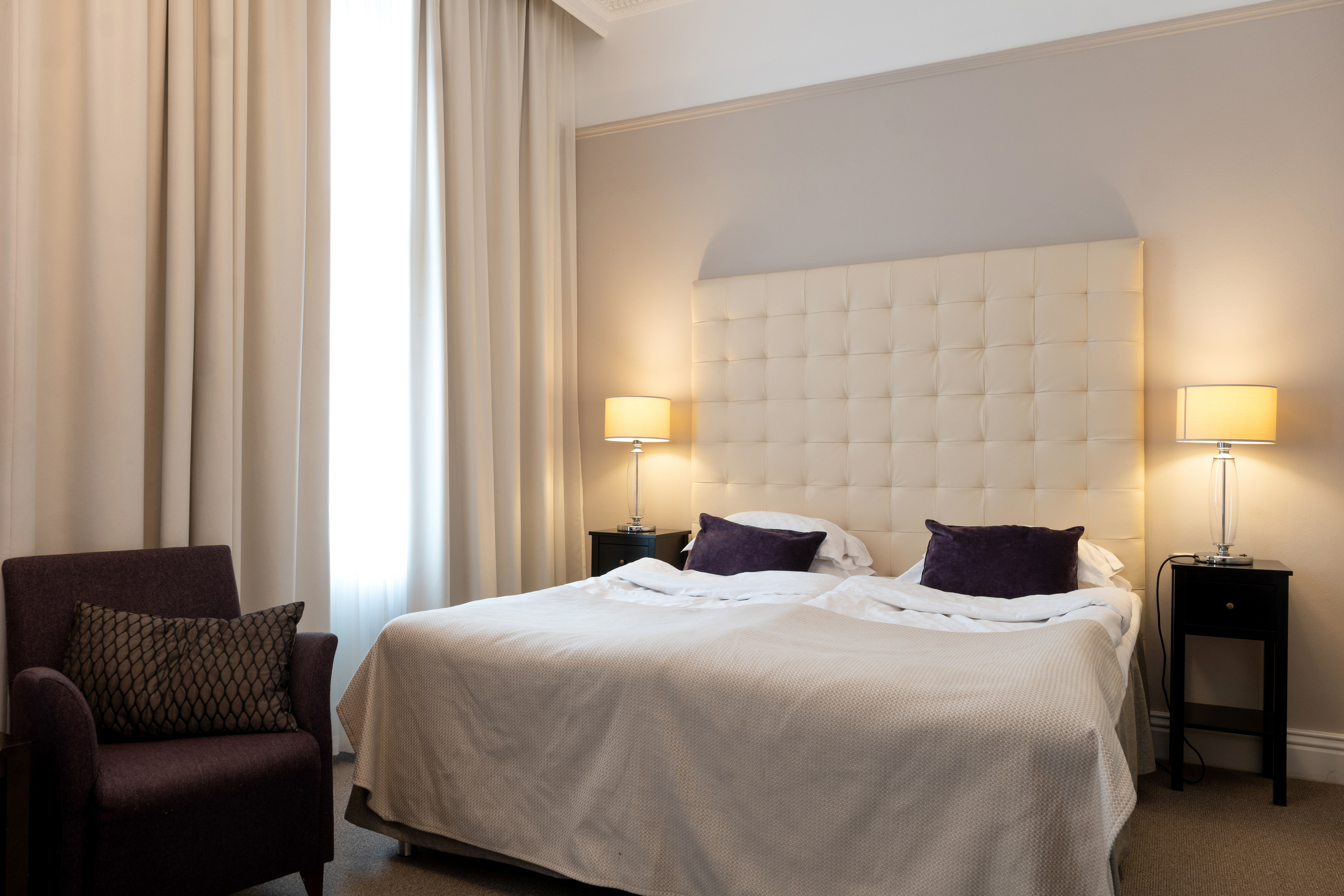 Bright hotel room with bed, white headboard and armchair