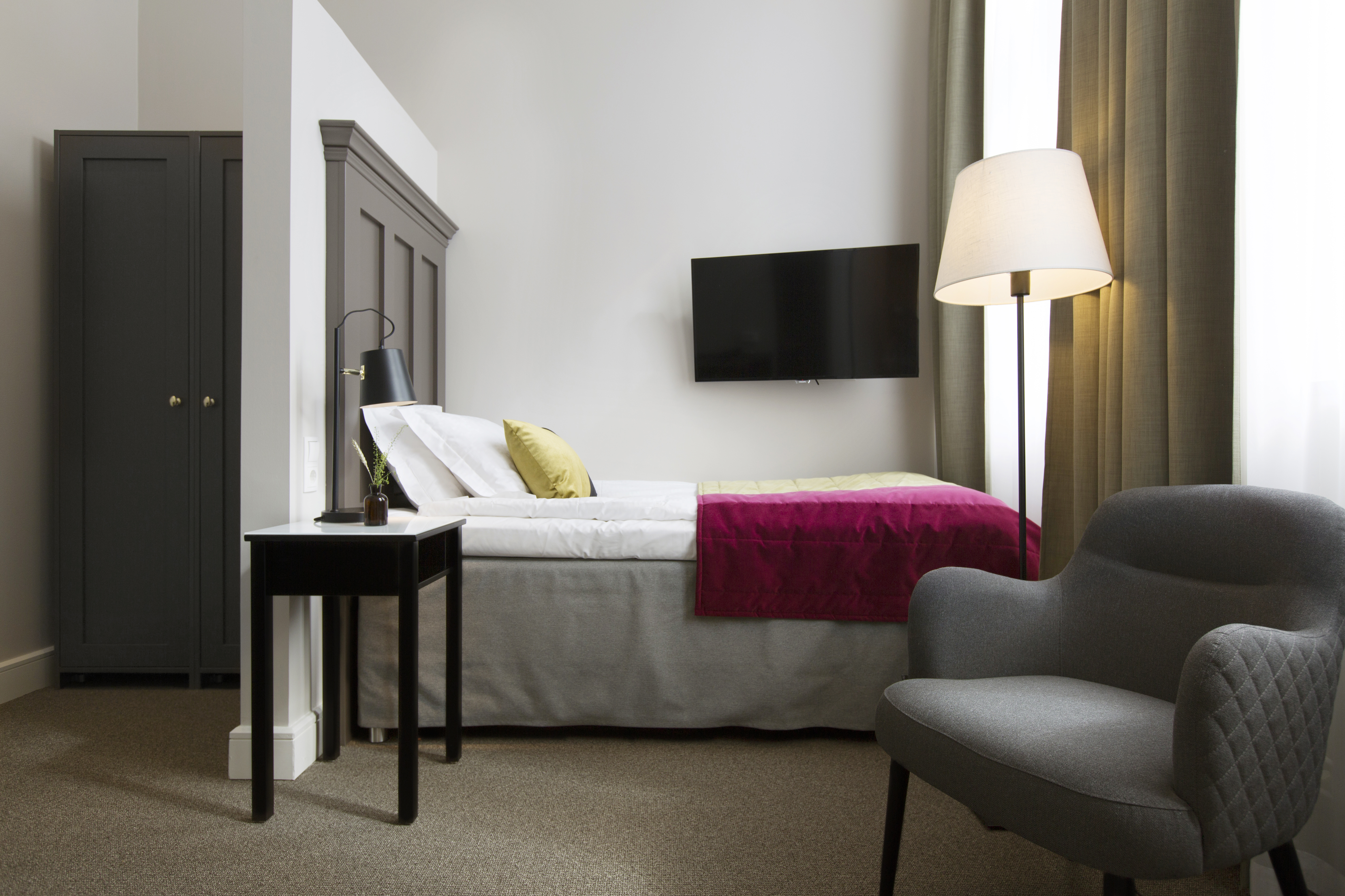 Bright hotel room with bed, wardrobe and armchair