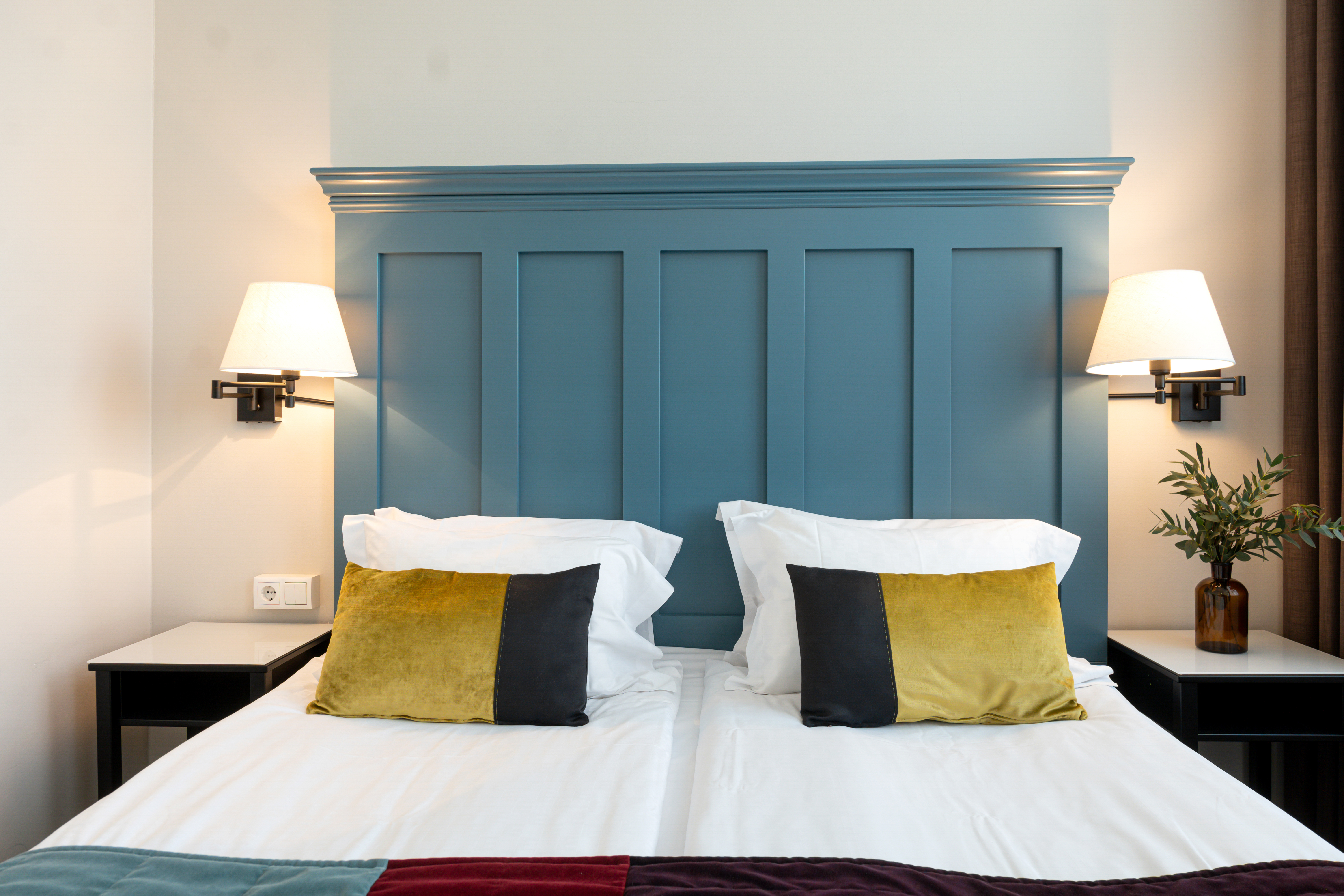 Bright hotel room with bed, large blue headboard and bedside lamps