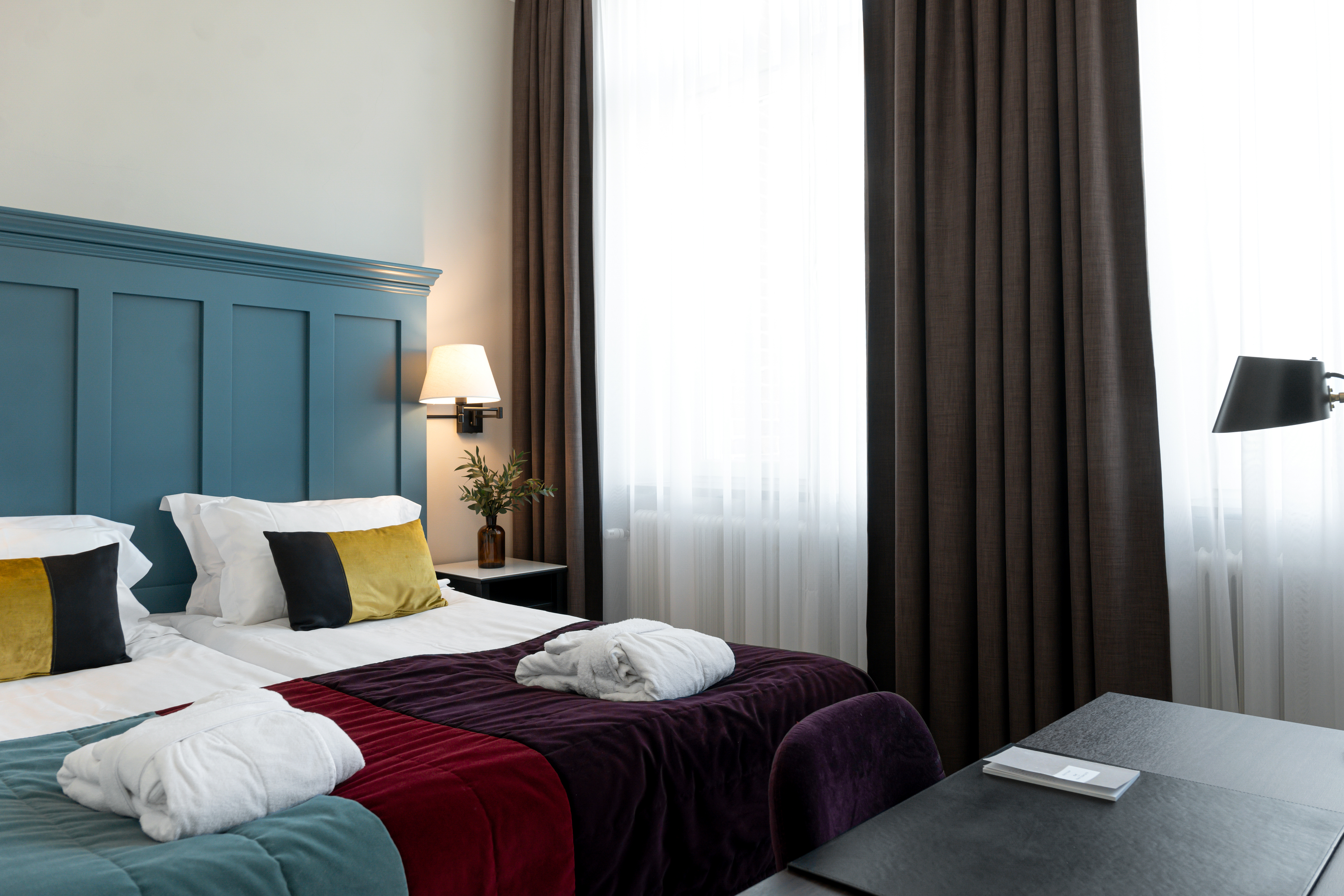 Bright hotel room with bed, large blue headboard and bathrobes